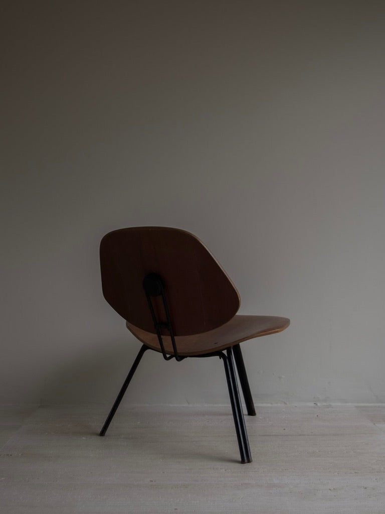 The Osvaldo Borsani - P31 by Bicci de' Medici, with a curved backrest and seat, rests against a light wall. Inspired by Italian Mid-Century design, it exudes timeless elegance similar to Tecno furniture's Borsani chairs, featuring black metal legs on a light floor.