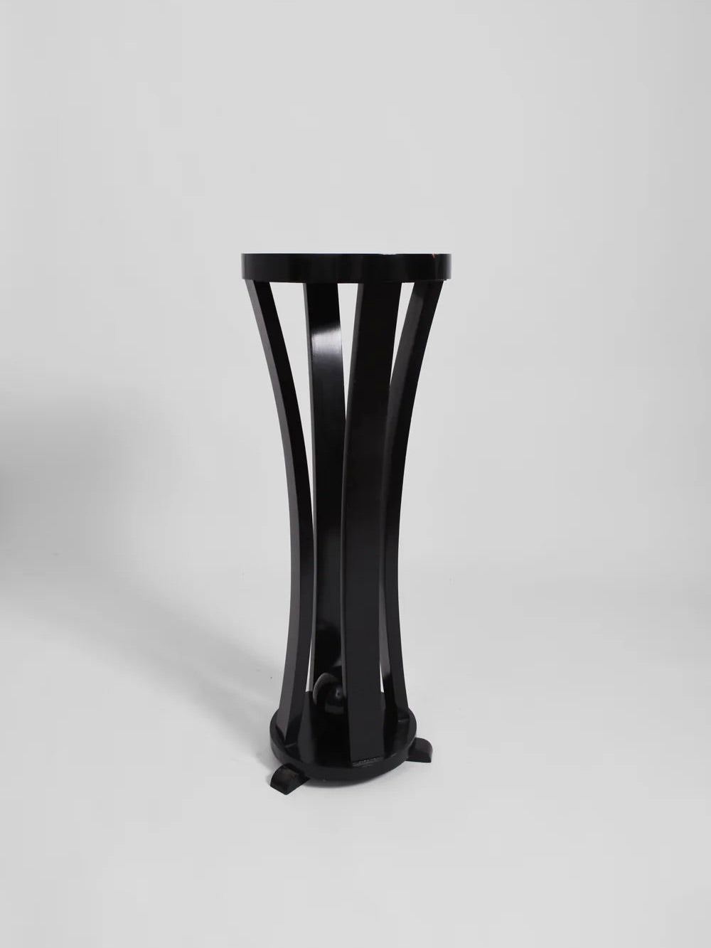 Barracuda Interiors' Pair of Black Wooden Pedestals captures the elegance of 1960s France, with its sleek circular top and gracefully curved slats forming the base, beautifully showcased against a plain white background.