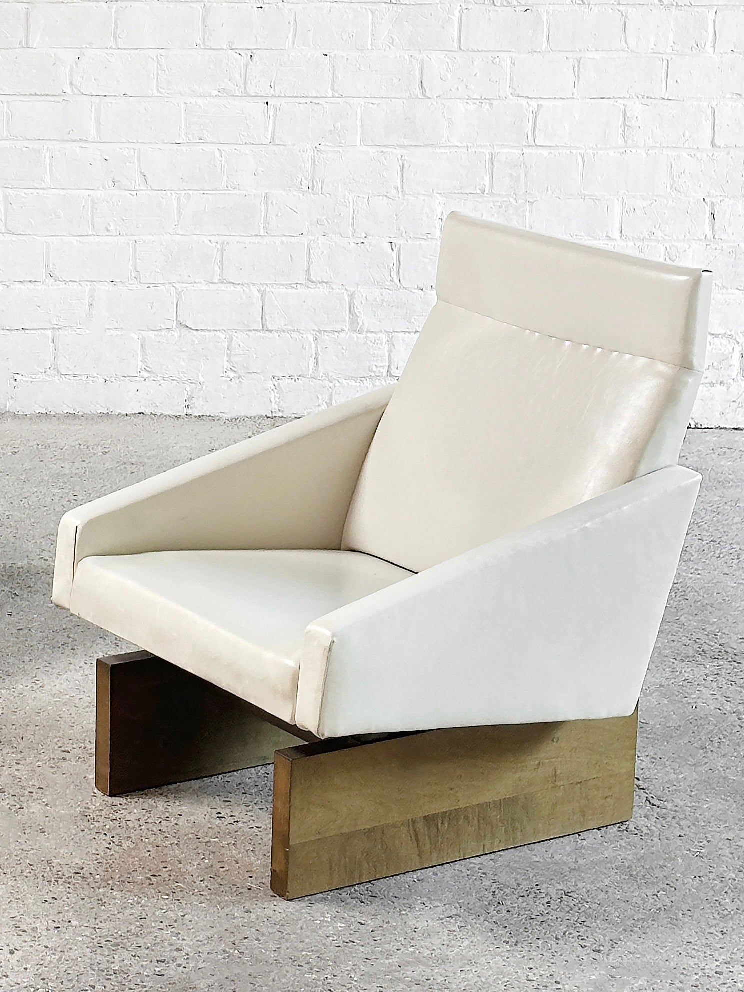 A French Modernist Sofa Set in white leather from the 1950s by Introverso sits on a concrete floor, highlighting its mid-century design with a wooden base and eco-leather upholstery against a white brick wall.