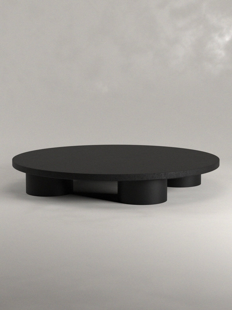 Discover Siete Studio's Totem Coffee Table, a minimalist masterpiece featuring a round black top and three cylindrical legs, meticulously handcrafted from solid walnut. This elegant piece blends function and style against a light gray backdrop.