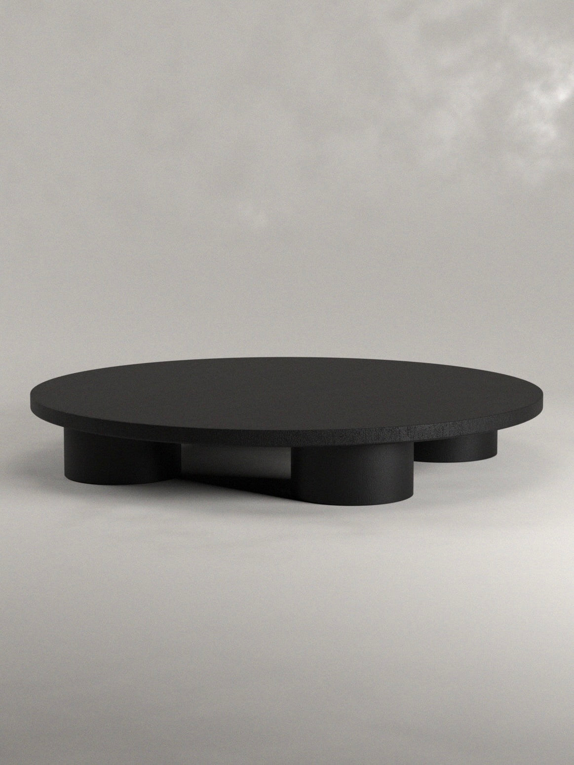 Discover Siete Studio's Totem Coffee Table, a minimalist masterpiece featuring a round black top and three cylindrical legs, meticulously handcrafted from solid walnut. This elegant piece blends function and style against a light gray backdrop.