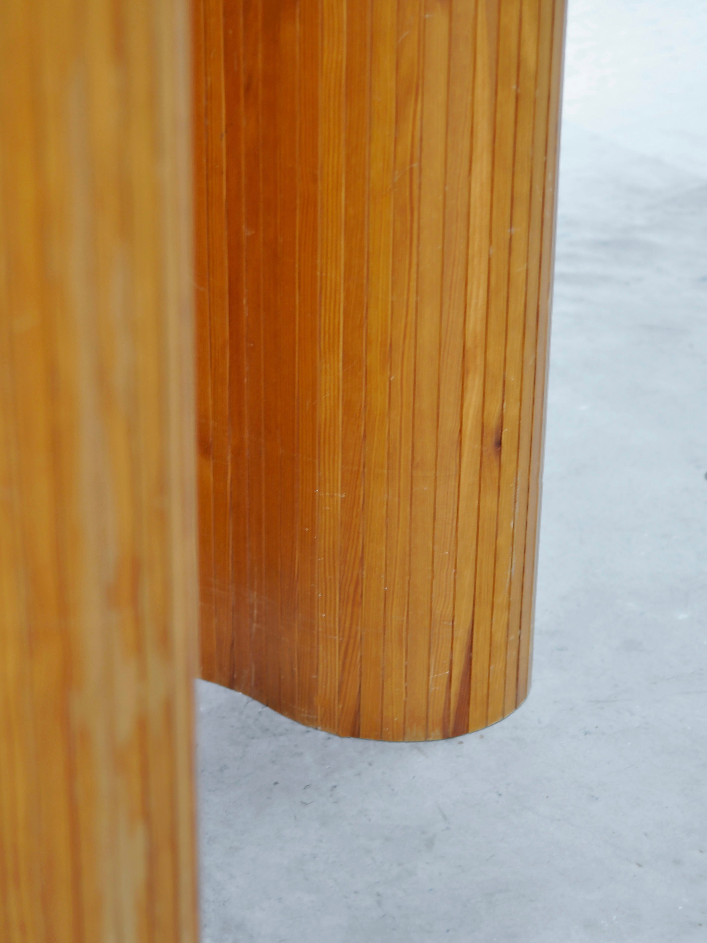 A close-up of the Room Divider by Jomaine Baumann from the 1940s, designed by Introverso. Featuring a smooth, light brown wooden finish with vertical grooves in a French Art Deco tambour style, it stands gracefully against a pale gray background.