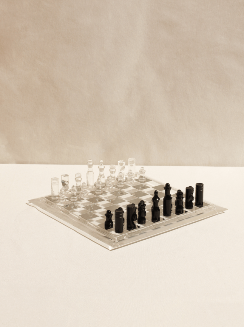 A Boga Avante Shop acrylic chess board with frosted and clear pieces, arranged and ready for play, on a pale backdrop featuring a modernist design.