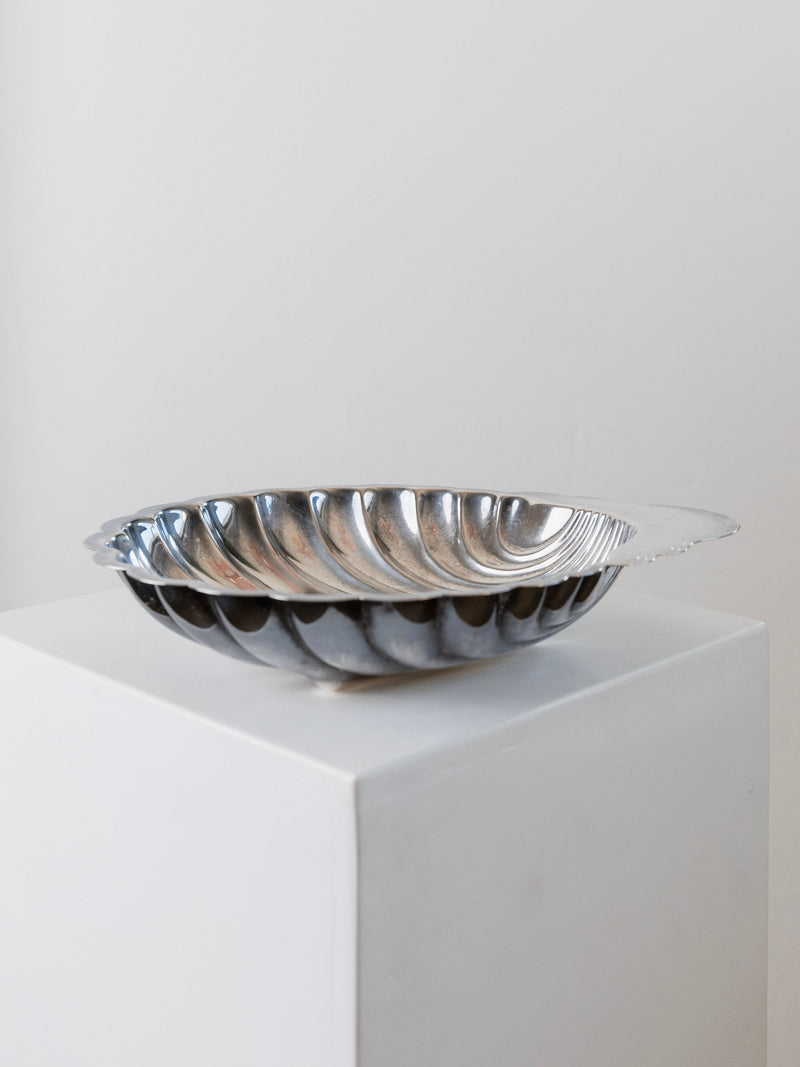 A stunning Silver Plated Vintage Shell Shaped Bowl by Bottega Jacobs is showcased on a white pedestal against a simple backdrop. Its fluted, spiral design enhances the elegance of this Italian table decoration, reminiscent of a vintage shell-shaped bowl.