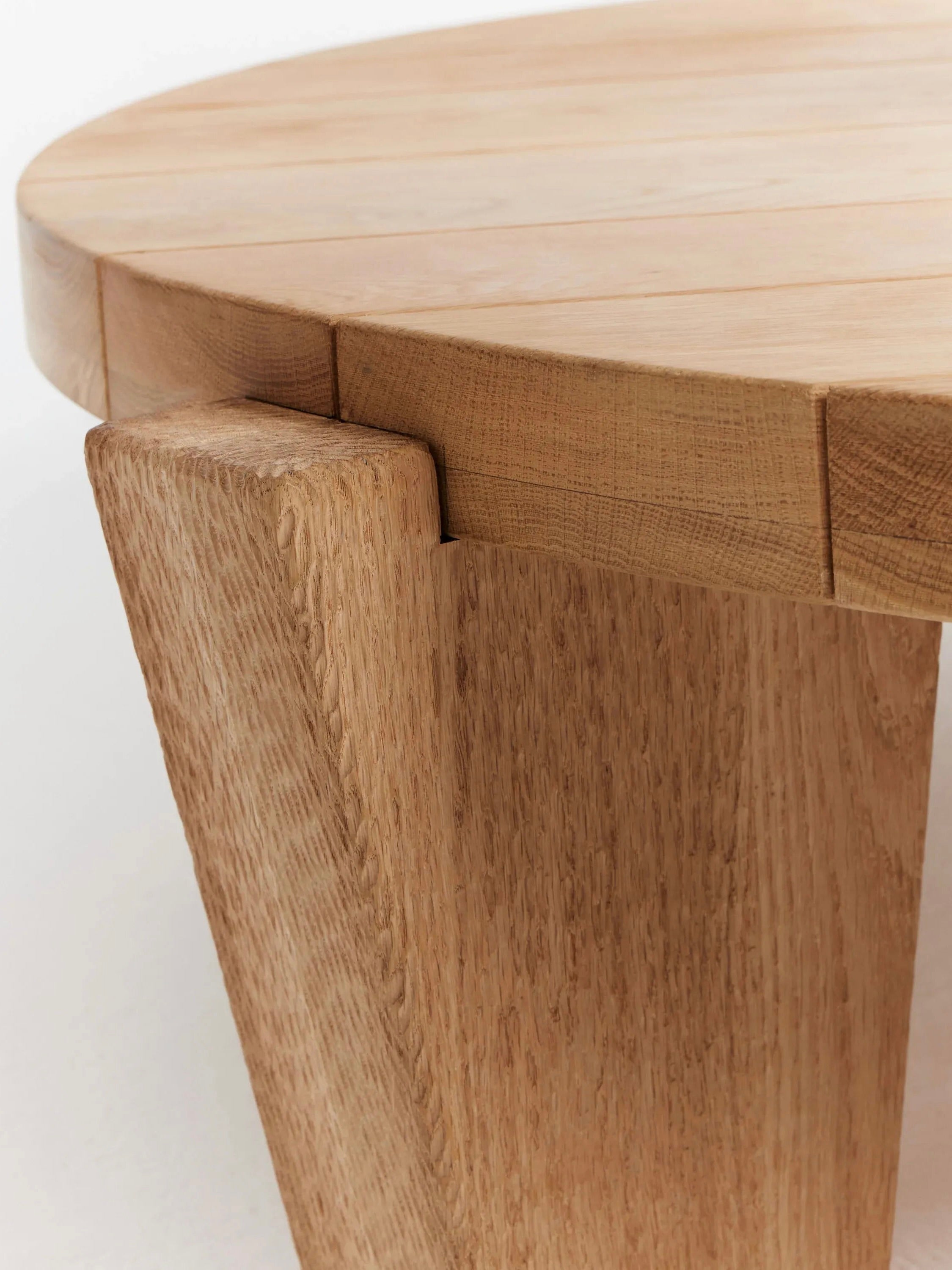 Close-up image of the "Peniche" Coffee Table in Oak by Project 213A, handmade in Portugal. It features a thick solid oak tabletop with sturdy angled legs, showcasing natural grain patterns and a smooth, polished finish. The legs have a unique inset design where they meet the tabletop.