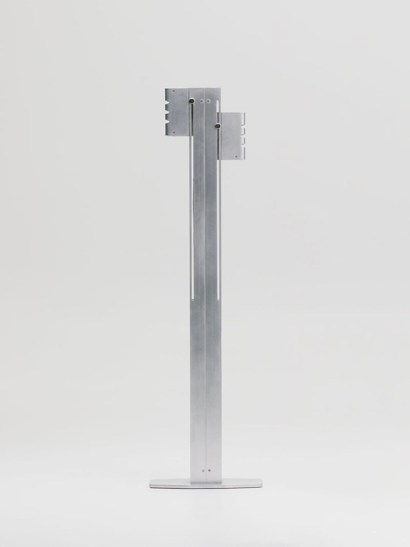 The Marquel Williams Beam Floor Lamp, handcrafted with a sleek metallic design and minimalist elegance, features an architectural style with vertical grooves, a rectangular base, and two brackets near the top against a plain white background.