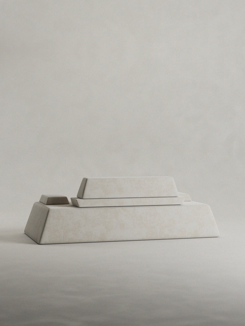 The 'Calakmul' Sofa by Siete Studio features three rectangular, pale beige stone blocks of varying sizes, reminiscent of an ancient pyramid. They are set on a light, neutral background, forming a minimalist and geometric design.