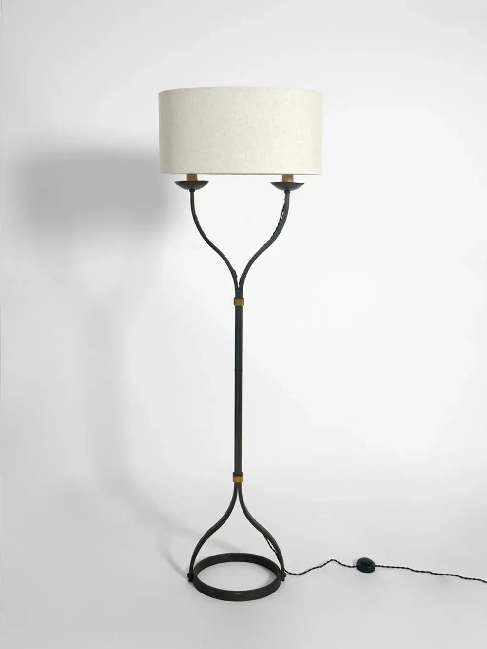 Introducing the Iron Floor Lamp, 1960s by Barracuda Interiors: This elegant lamp features a sleek black wrought iron frame with a circular base. Its dual-arm design harkens back to 1960s France, supporting a large cylindrical beige lampshade. A convenient black power cord with a foot switch completes its vintage-inspired look.