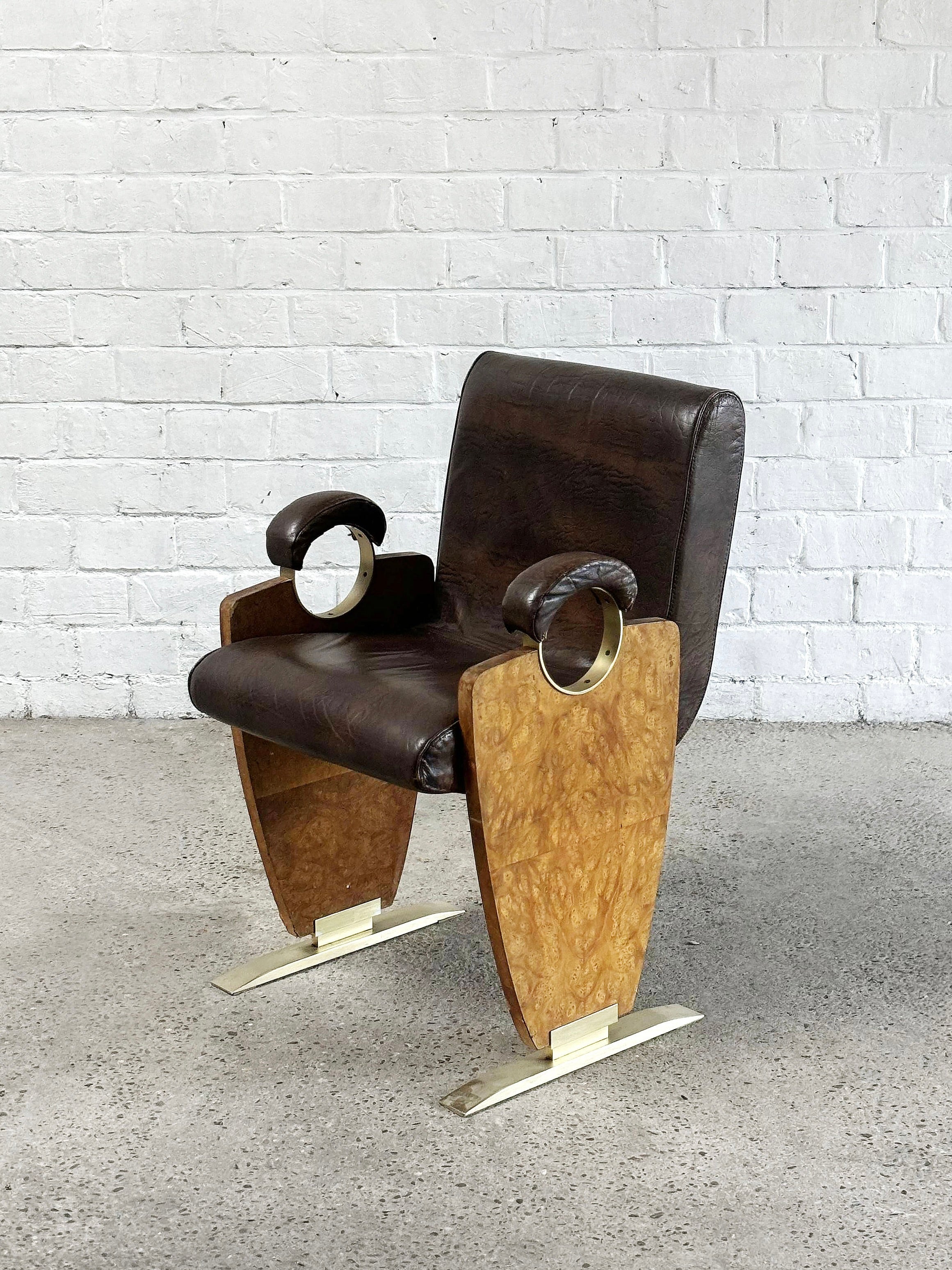 The Art-Deco Style Side Chair by Introverso, from the 1970's, showcases modern skai leather upholstery in brown, curved burl walnut wood armrests, and sleek metal legs, set against a white brick wall and concrete floor.