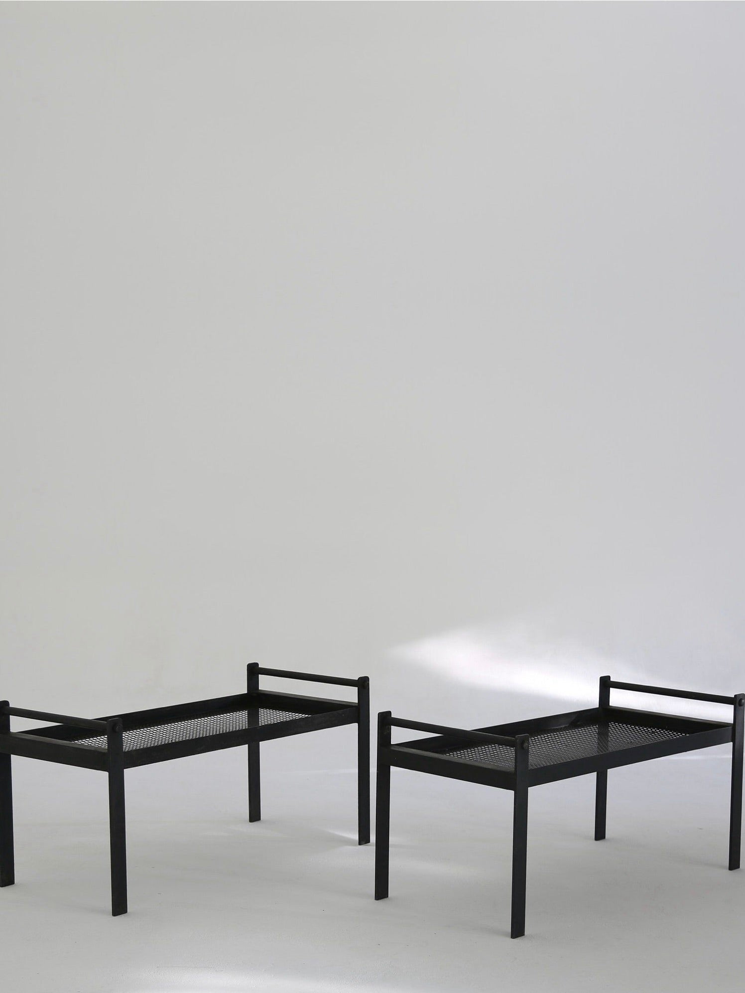 Two black rectangular benches from the Ancien et Jolie Modernist Lounge Set evoke Mathieu Mategot's style with metal mesh surfaces and a light gray backdrop. Soft shadows enhance their sleek steel-framed design and minimalist appeal.