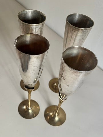 Four Maud Vaughan Mid-Century Mixed Metal Flutes stand elegantly on a light surface. With brass-plated stems and chromed cups, these closely arranged flutes exude a vintage charm, ready to toast any occasion.