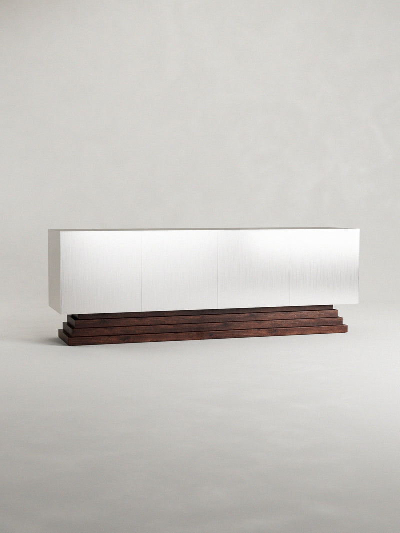 The 'Fragua' sideboard by Siete Studio features a sleek, minimalist design with clean white lines on a walnut base set against a neutral background, showcasing the contrast between its modern aesthetic and rich wood grain craftsmanship.