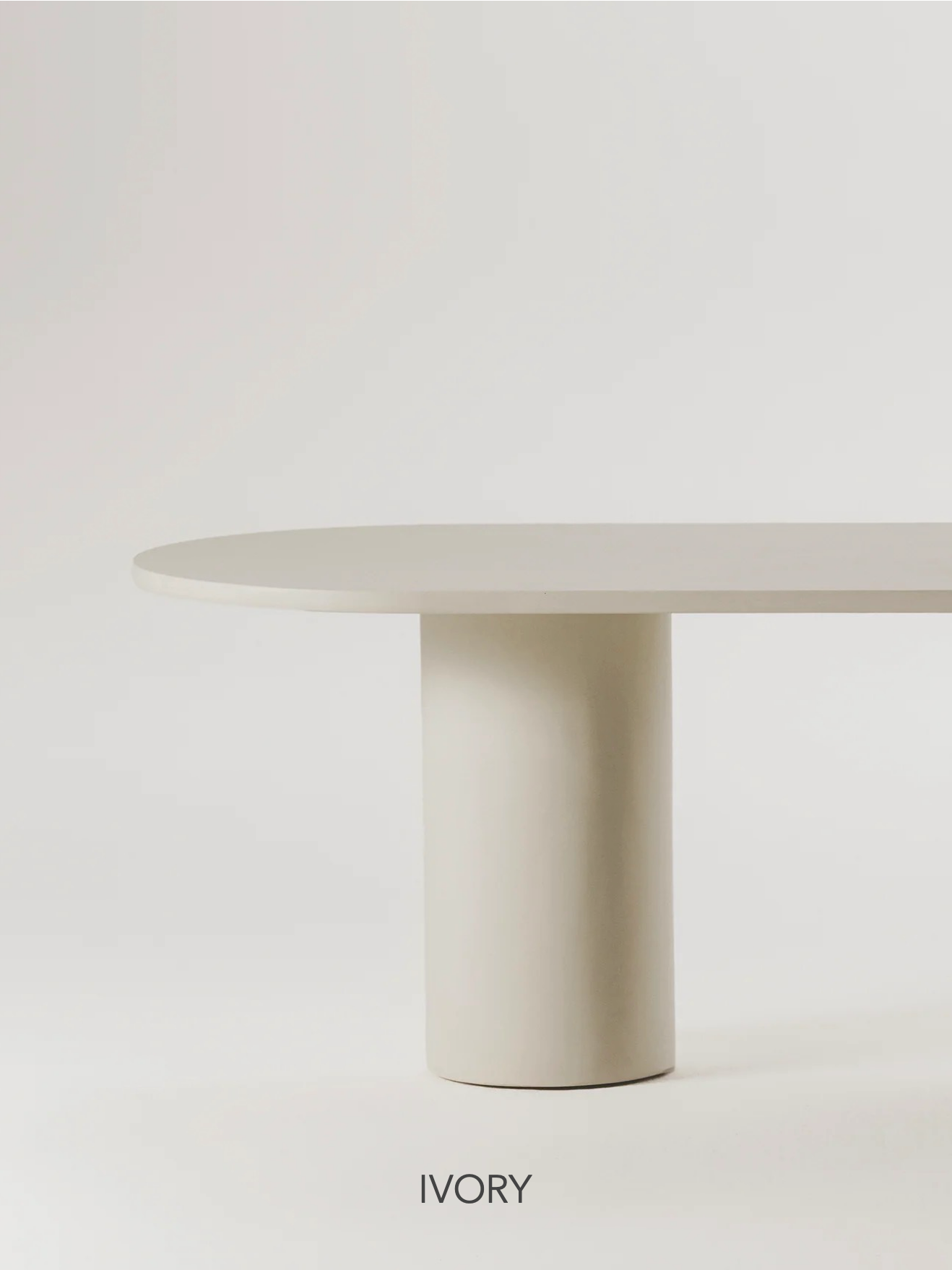 The Gio Dining Table by MarlotBaus features a minimalist design with an oval top and a cylindrical microcement base, all in an ivory hue. Set against a plain white background, the word "IVORY" is displayed at the bottom of the image, highlighting its sleek modern style.