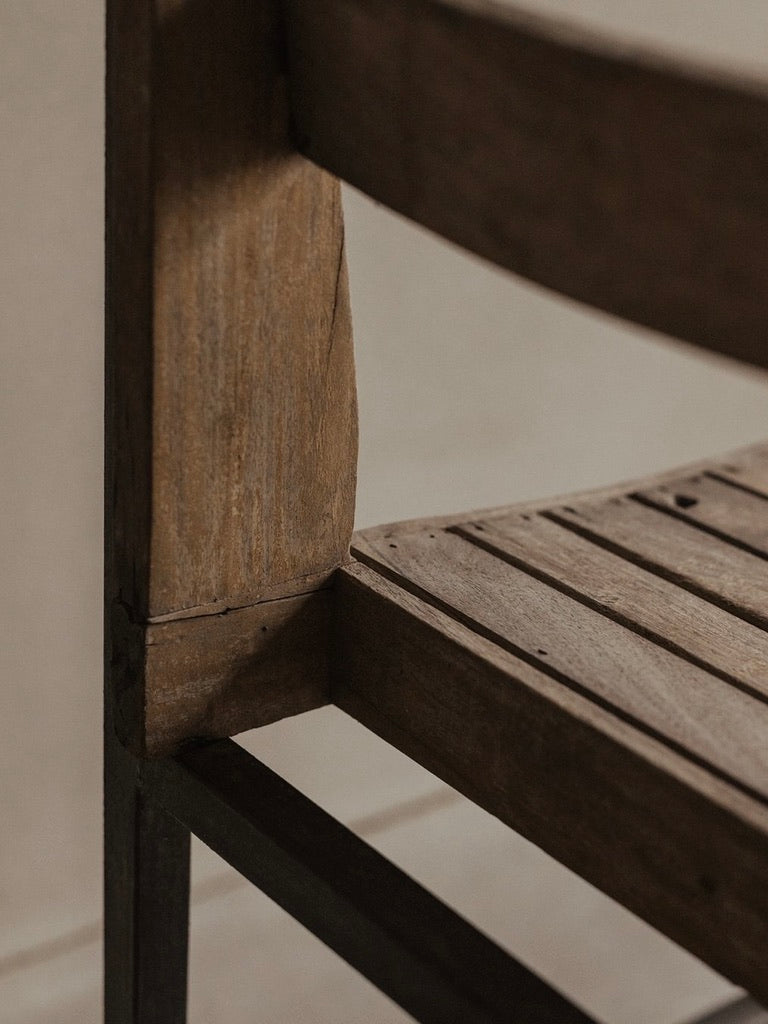 A close-up of the Bicci de' Medici Pierre Jeanneret Authentic PJ-SI-65-A chair showcases its vintage charm with a worn seat and sturdy backrest. The teak wood slats feature a rustic look with visible grain and slight wear, beautifully capturing the corner detail.