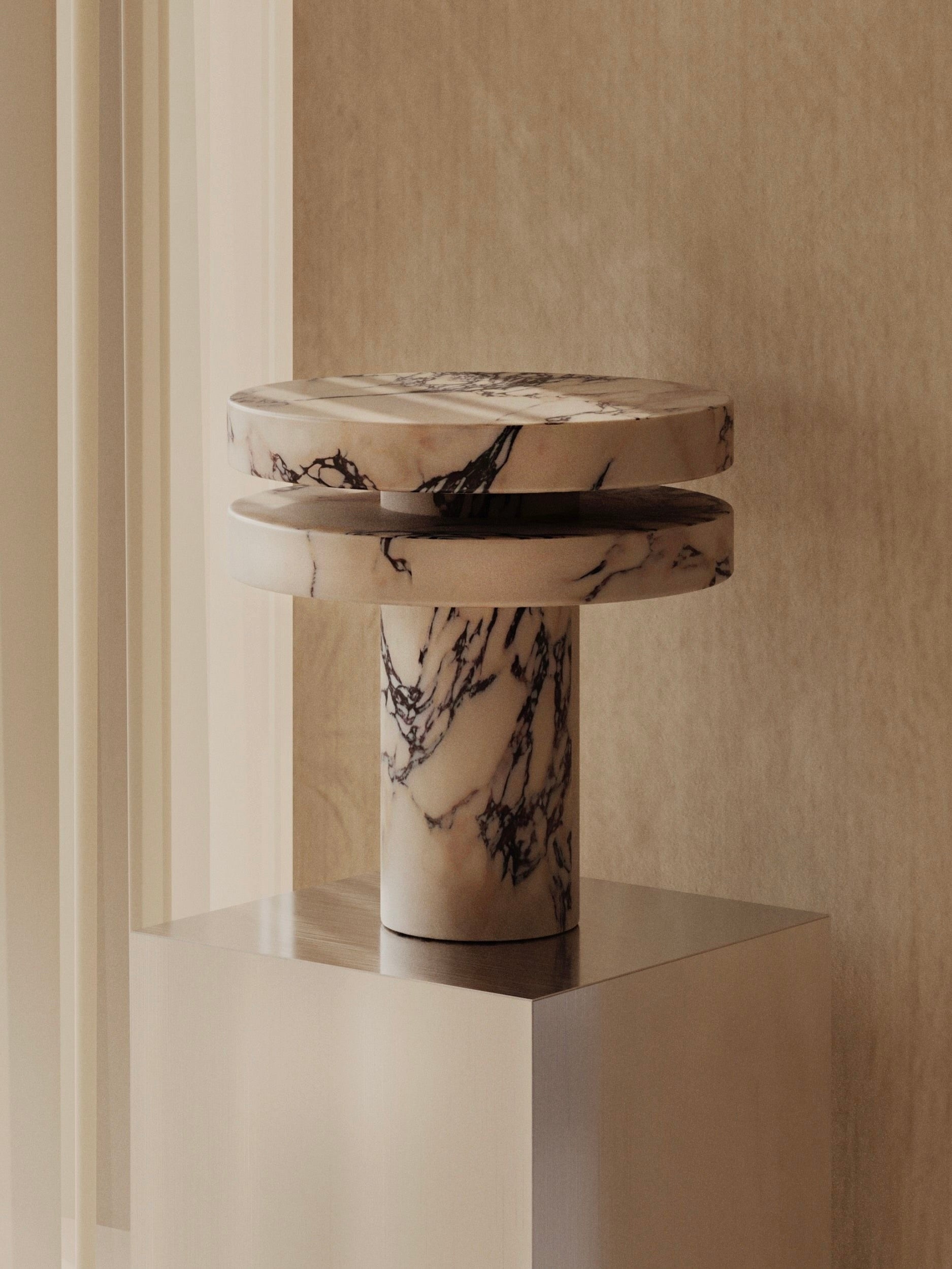 The 'M_014' Marble Table Lamp by Monolith is a modern sculpture featuring two circular platforms, a central column with elegant black veining, and subtle LED lighting. It's displayed on a wooden pedestal against a neutral textured background, perfectly blending modernity with brutalist design.