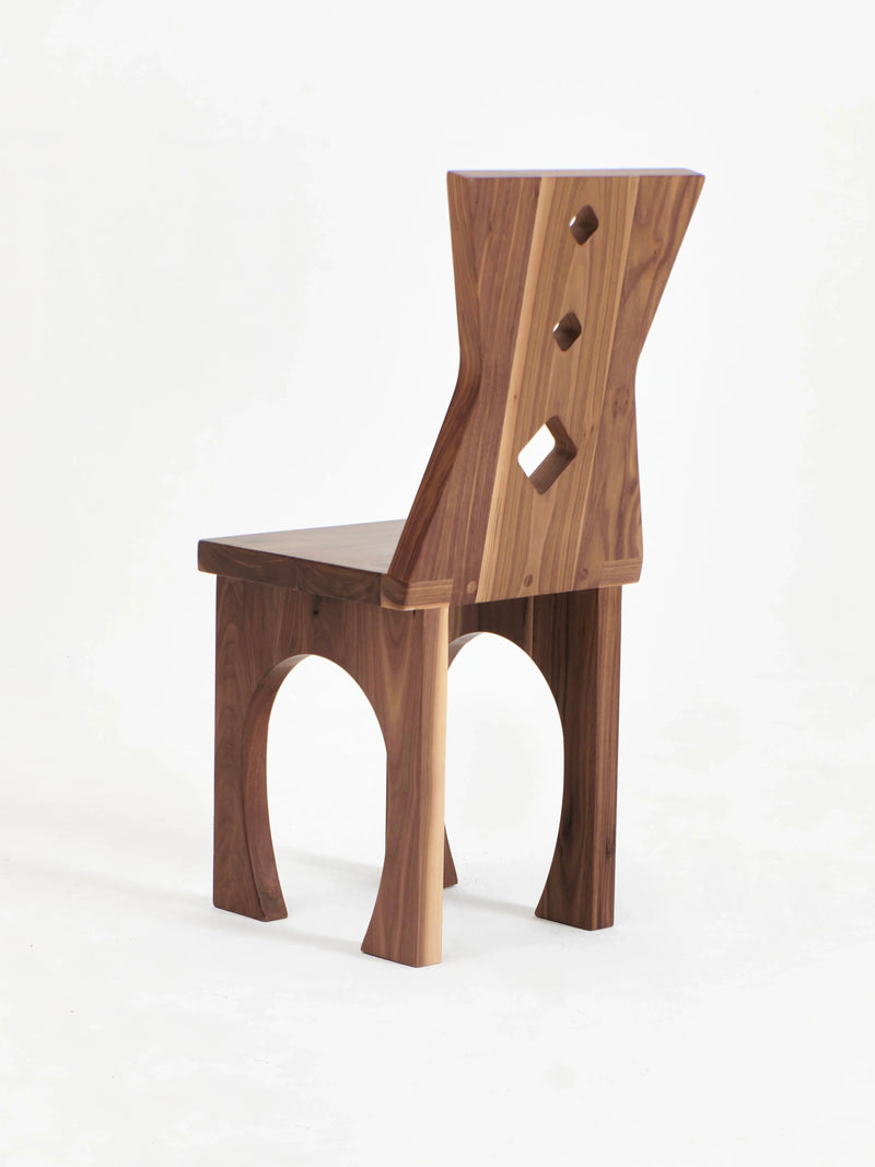 The Portugal Chair No 2 by Project 213A showcases a distinct backrest with three diamond-shaped cutouts. The chair boasts a minimalist design, featuring a flat seat and curved legs, all crafted from solid walnut with a rich, natural finish. Set against a plain white background, the chair's exquisite craftsmanship is perfectly highlighted.
