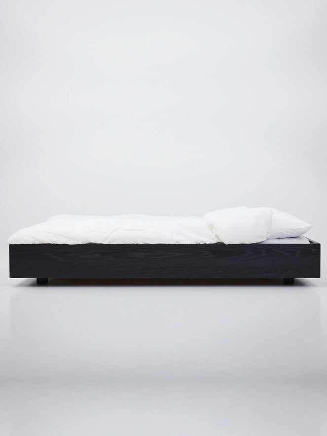 Black floating bed platform with white bedding, minimalist side profile view