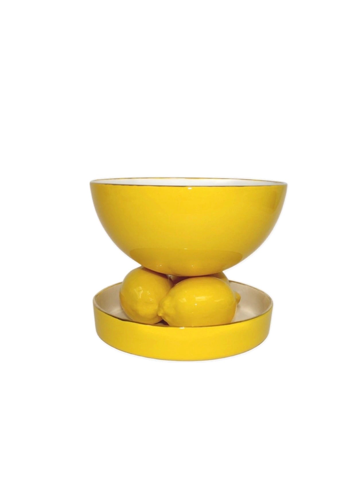 A vibrant yellow Lemon Coupe Gianni by Villa Arev is delicately balanced on top of two yellow lemons placed in a matching shallow dish. Handmade in Paris from glazed earthenware, the entire arrangement is set against a plain white background.