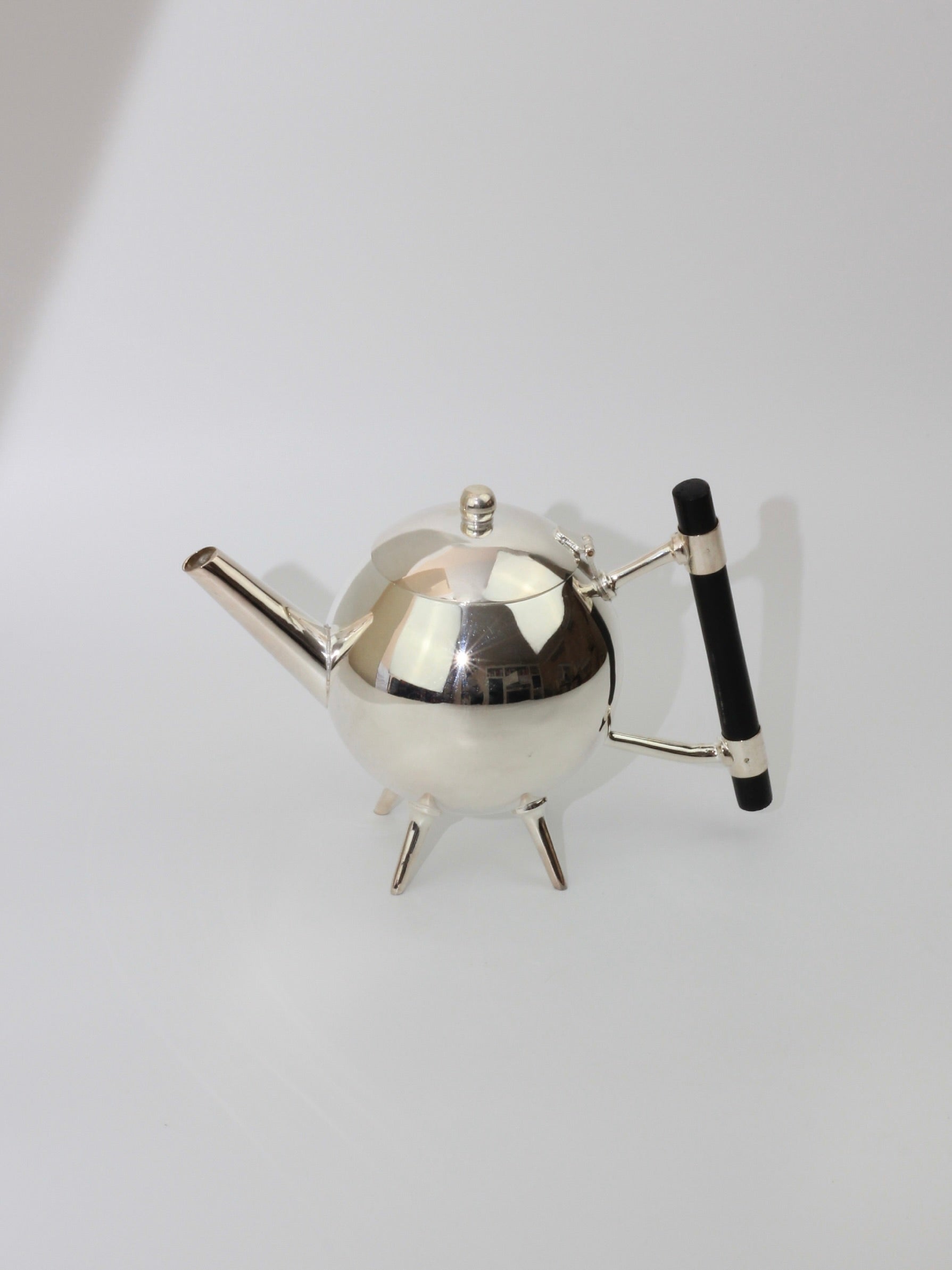 Introducing the Christopher Dresser's Tea Pot by Boga Avante Shop: a sleek, modern silver-plated teapot with a geometric design and an ebonized wood handle. This teapot boasts a short spout and stands on three pointy legs, all set against a plain, light background—exemplifying Dr. Christopher Dresser's innovative style.