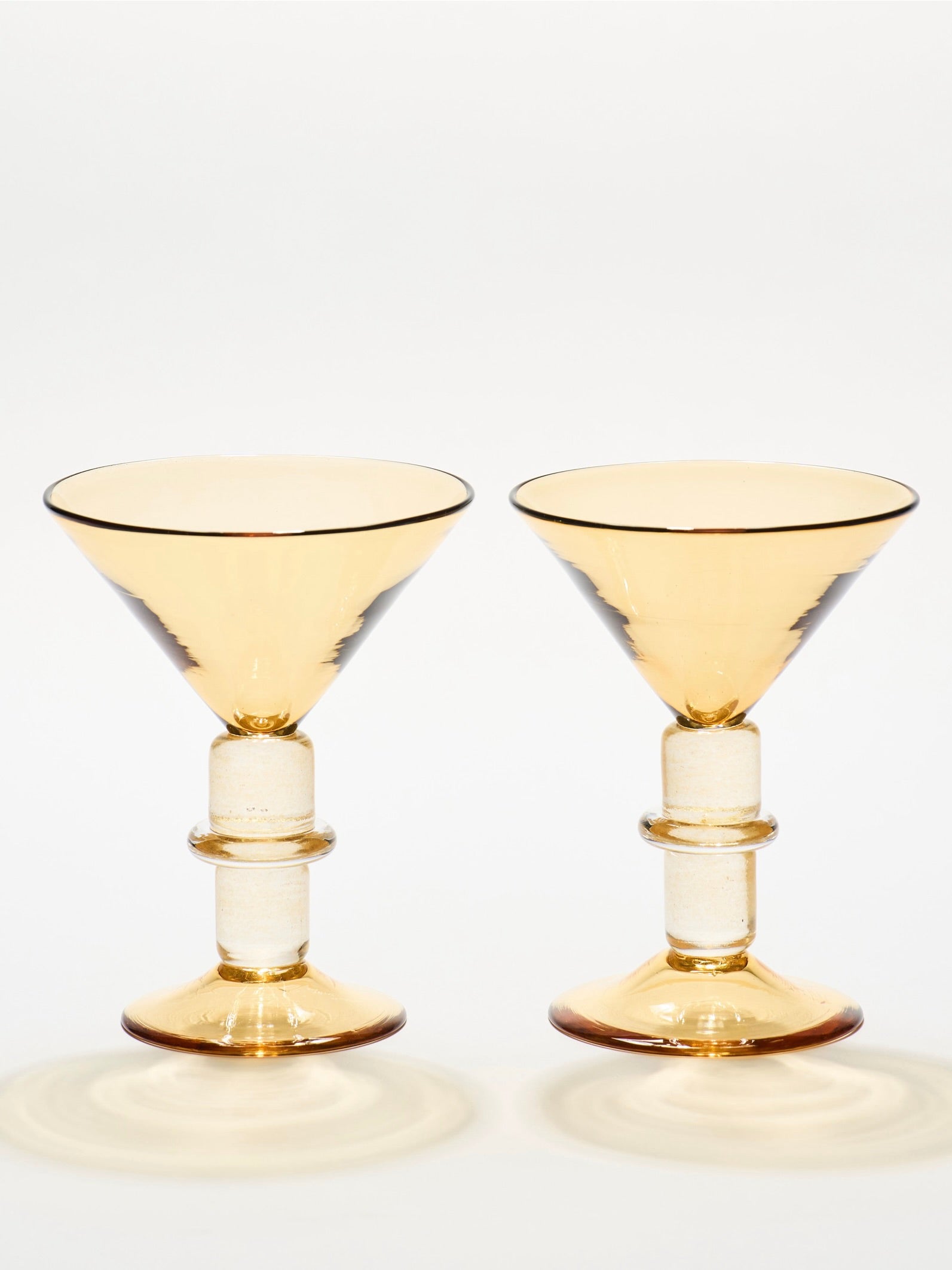 The New York Martini Glass in Whisky by Gather features two amber-colored glass goblets with wide, shallow bowls and cylindrical-shaped stems. Hand-blown, they add elegance to the sophisticated collection.