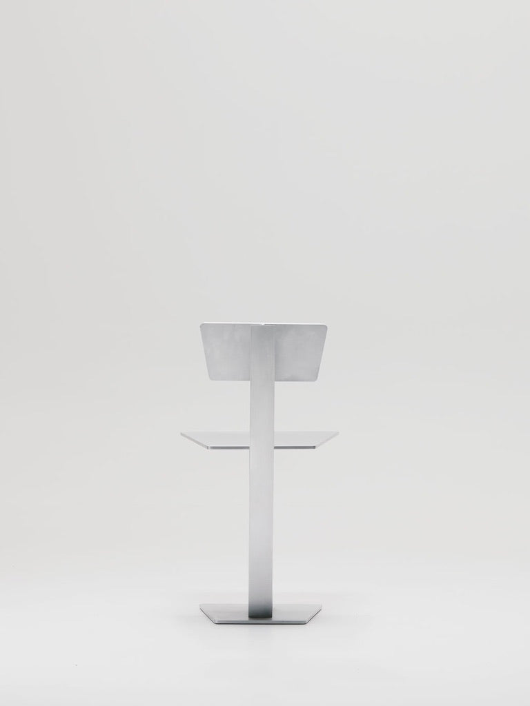 The Beam Chair by Marquel Williams features a sleek, angular design reminiscent of architectural buildings, set against a plain white backdrop.