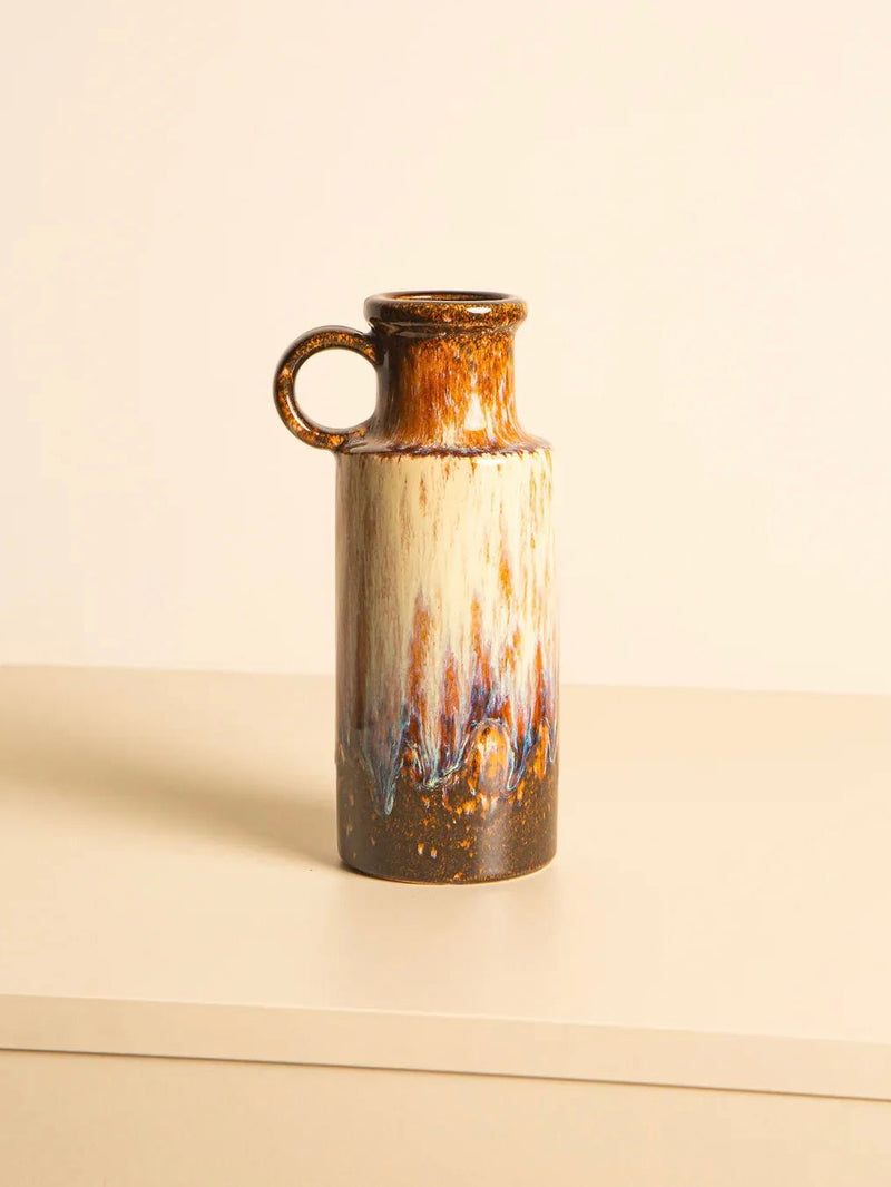 A tall Scheurich Ceramic Vase 80s by Treaptyque, showcasing a glossy multicolored glaze with earthy tones and brush-like patterns and featuring a single handle on the upper left side, is elegantly displayed on a light-colored surface against a neutral background, capturing the enduring style of 1980s Germany.