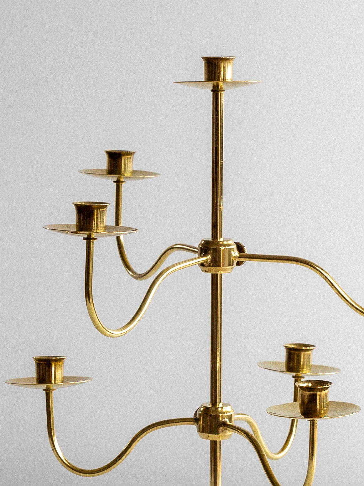 A close-up of a brass multi-armed candle holder against a neutral background. This Medium Mid-Century Brass Candelabra by Spigel features an intricate design with multiple curved branches, each supporting candle sockets, creating an elegant and sophisticated appearance, embodying timeless style.