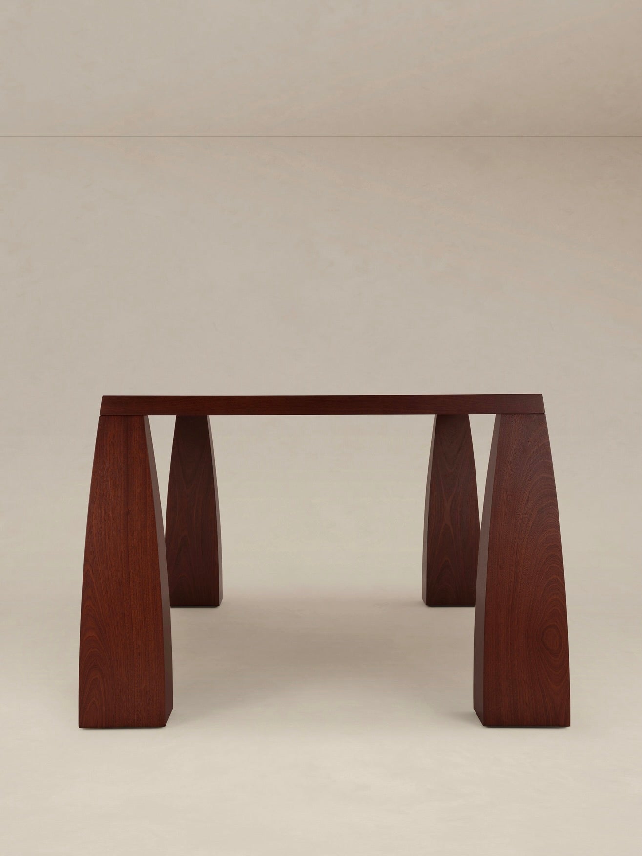 The "Khram" Dining Table by AÈDE Studios, a minimalist wooden piece with a smooth dark finish and four wide, flat legs, features a subtle trapezoidal shape against a plain, neutral background.