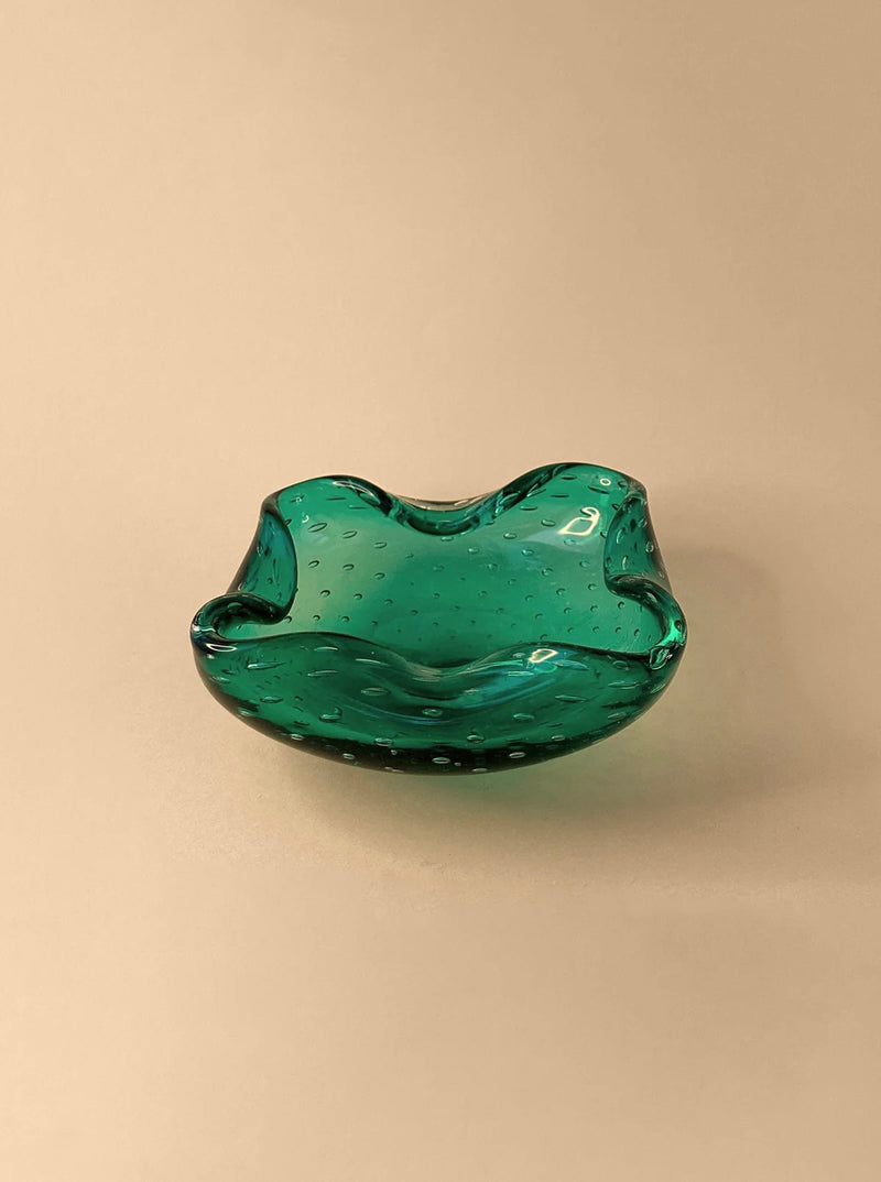 A Mint Green 1960s Murano Ashtray by Dodo Vintage, featuring a wavy, scalloped edge and a smooth, glossy surface, sits on a beige background. This exquisite bowl-like ashtray showcases the bullicante technique with small air bubbles trapped within the glass, adding texture and depth to its appearance.