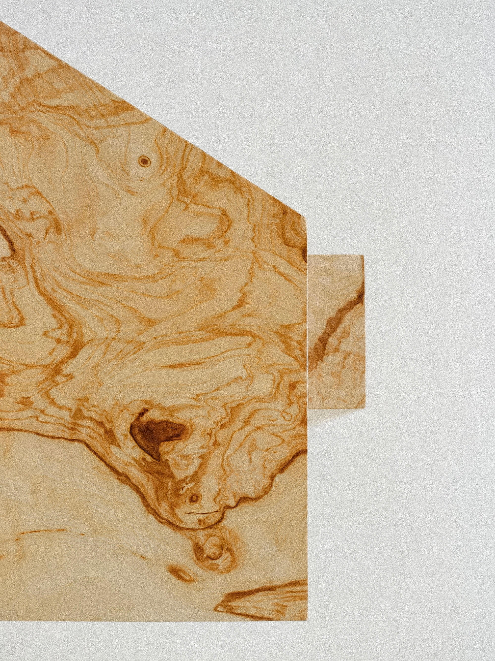 Close-up of a wooden surface showcasing a natural, swirling grain pattern. A rectangular wooden piece, resembling the SSS01W Stool by sashaxsasha, extends from the main section, offering a geometric contrast to the organic lines. The wood tone is light brown with darker accents.