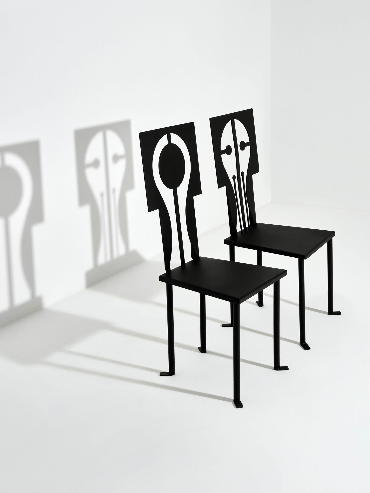 The Epona Chair in Iron and Black Powder Coat from Animate Objects collection showcases abstract cutout backs, casting artistic shadows on a white background.