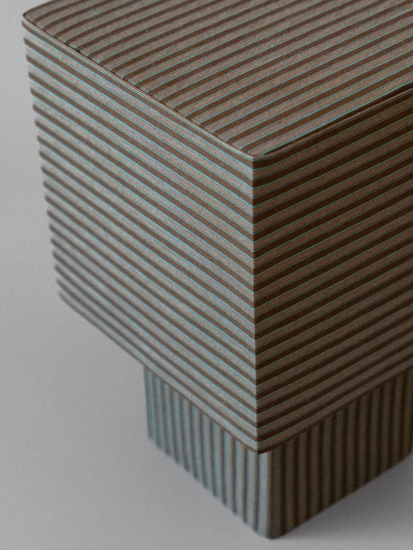 An up-close view of "La Petite Boîte" - Brown Stripes Table Lamp by mattina moderna showcases its handcrafted, textured rectangular design featuring horizontal ridges. The surface's alternating light and dark stripes add a playful touch against the plain background.