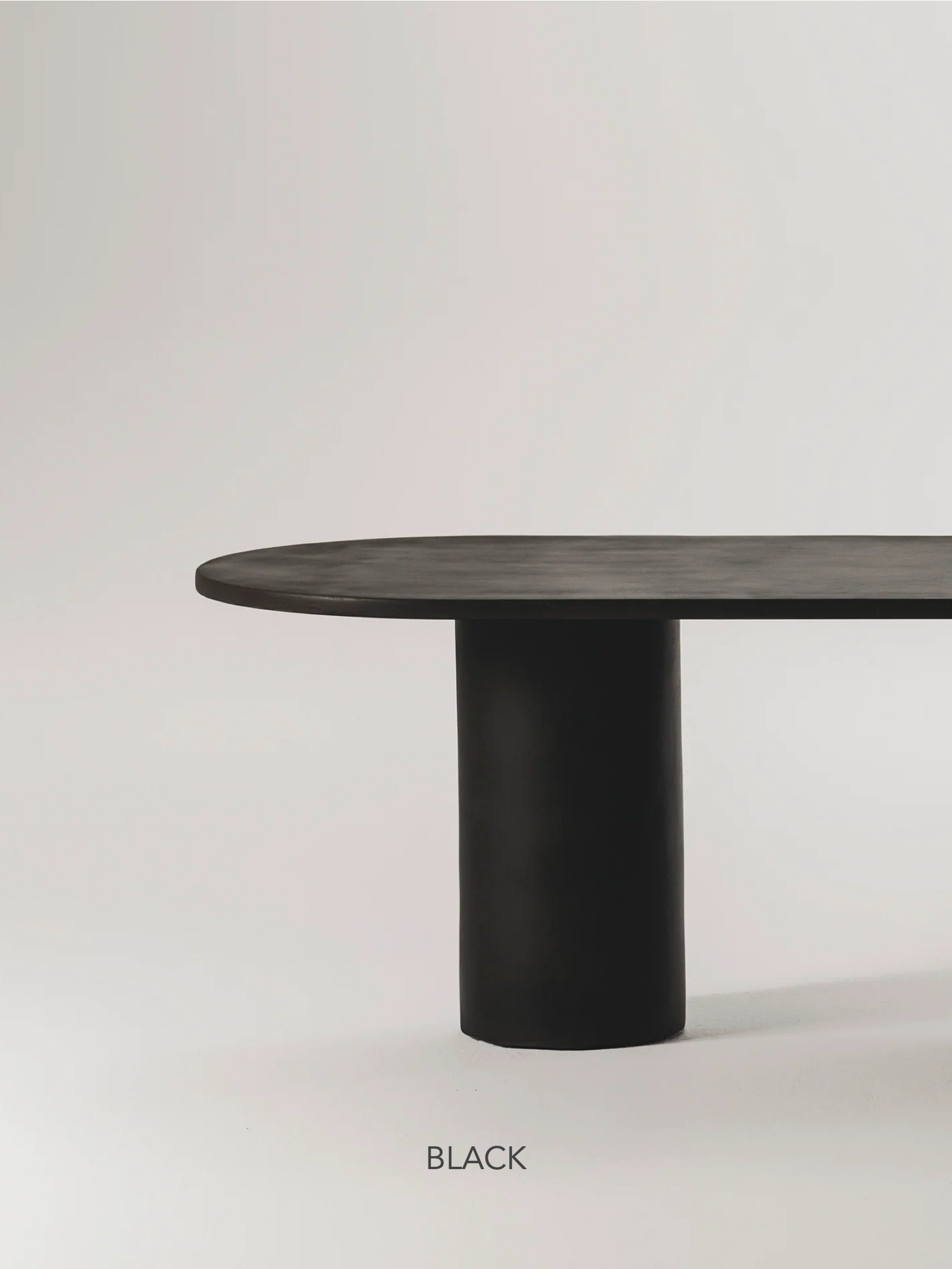 The Gio Dining Table by MarlotBaus, featuring a modern microcement design with a cylindrical base and oval top, is showcased against a minimalistic light-colored background with the word "BLACK" elegantly written underneath.