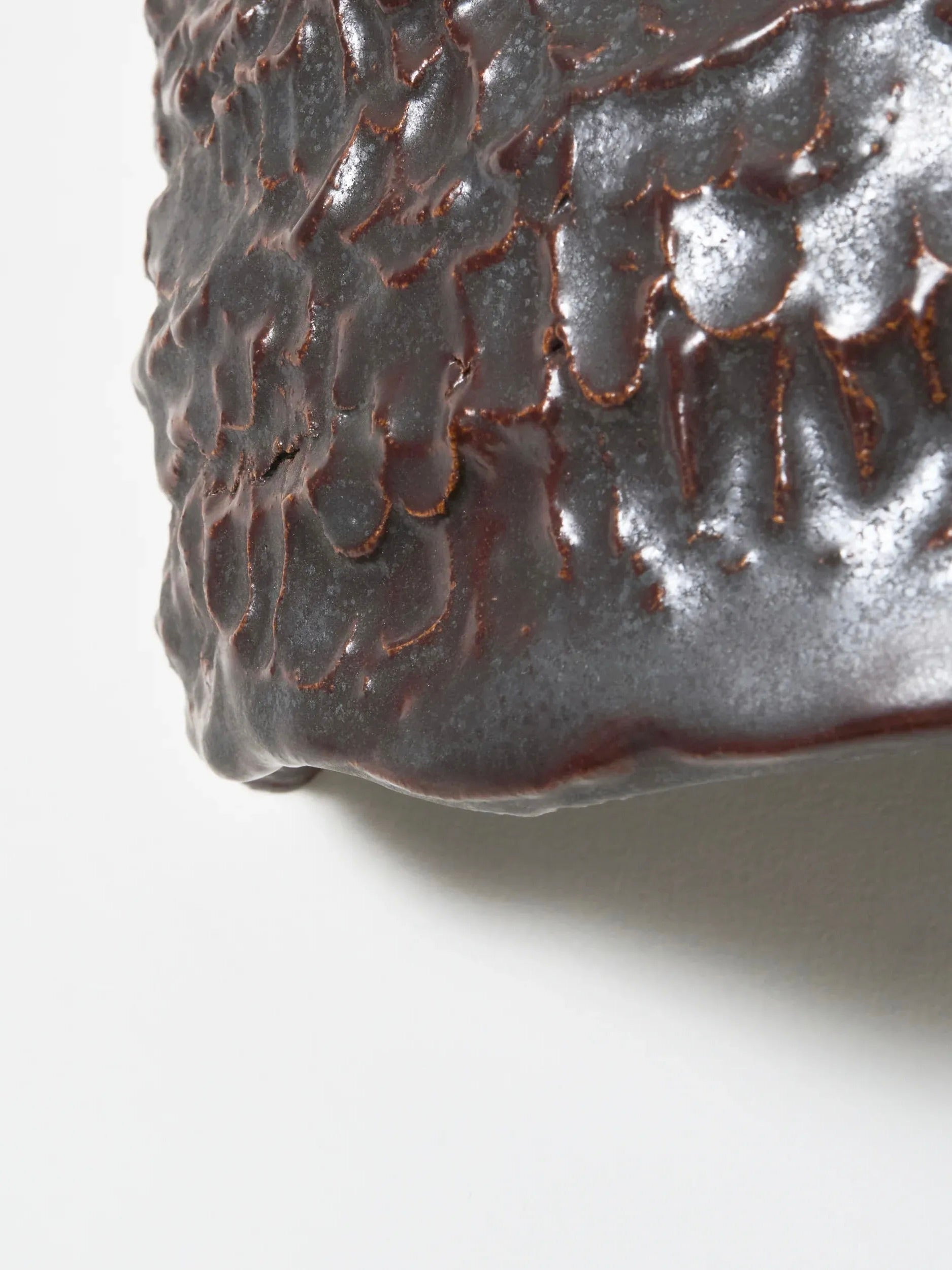 Close-up of an artisanal ceramic surface with a dark, textured glaze. The handmade finish produces an uneven, organic pattern akin to scales or leaves. Irregular edges add to its natural charm, making it ideal for the Project 213A Casa Wall Light No3 design.