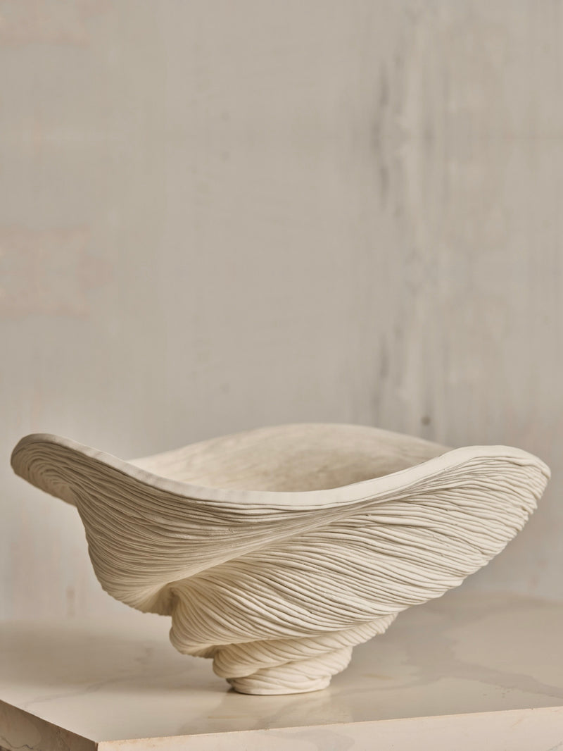 The Soucy Shop's Porcelain Bowl, with its swirling, textured ridges crafted from hand-rolled porcelain coils, features an organic shape reminiscent of natural formations. This unique and elegant piece showcases exquisite artistry in its one-of-a-kind design.