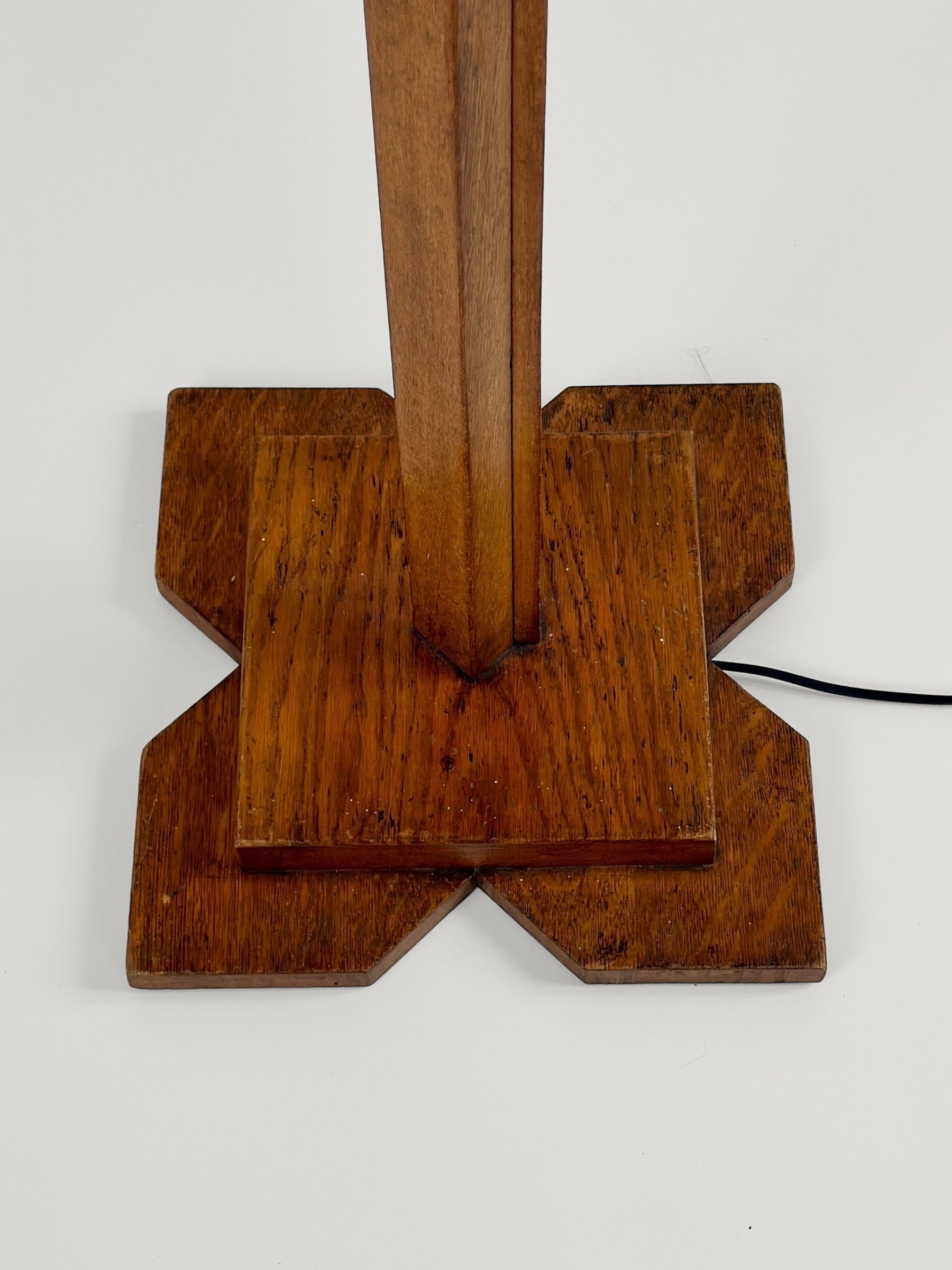 The image displays the wooden base of the Figuresdesign Art-Deco Floor Lamp, dating back to circa 1930. The cross-shaped base features a raised center where the lamp's column connects. A power cord emerges from the polished, intricately carved wood, highlighting its beautiful grain patterns.