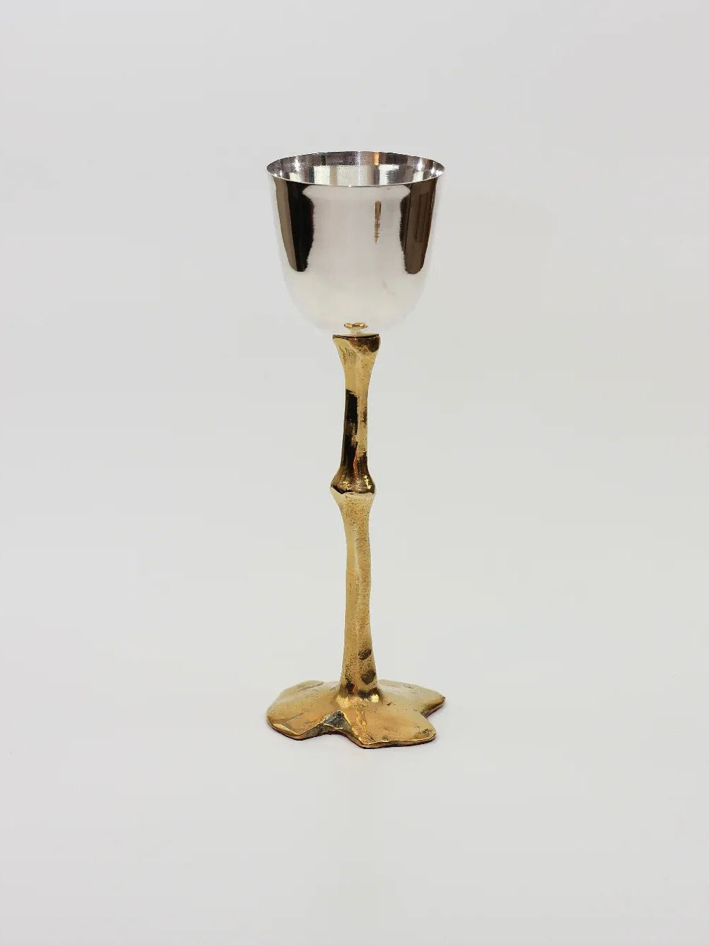 Introducing the Brutalist Goblets by Boga Avante Shop: A silver goblet featuring a hand-sculpted brass stem and base, artfully designed to mimic a slender branch, elegantly displayed against a simple white backdrop.