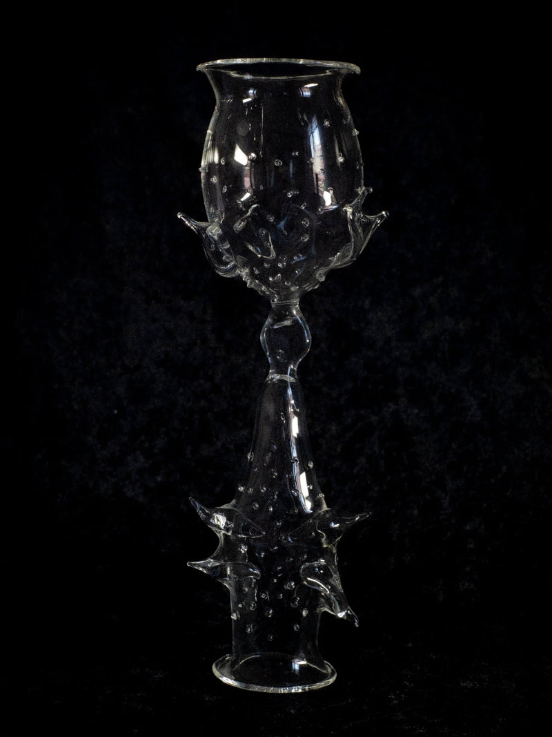 Elegant and intricately designed, the Objects of Affection_Besos Decorative Glass by Pia Glassworks features sculpted spikes along its stem and bowl, casting an enchanting aura against a dark backdrop.