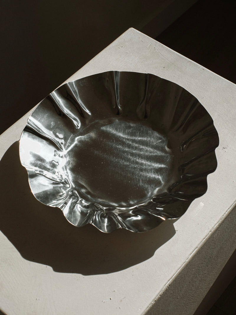 Large chrome folded bowl with scalloped edges on concrete surface