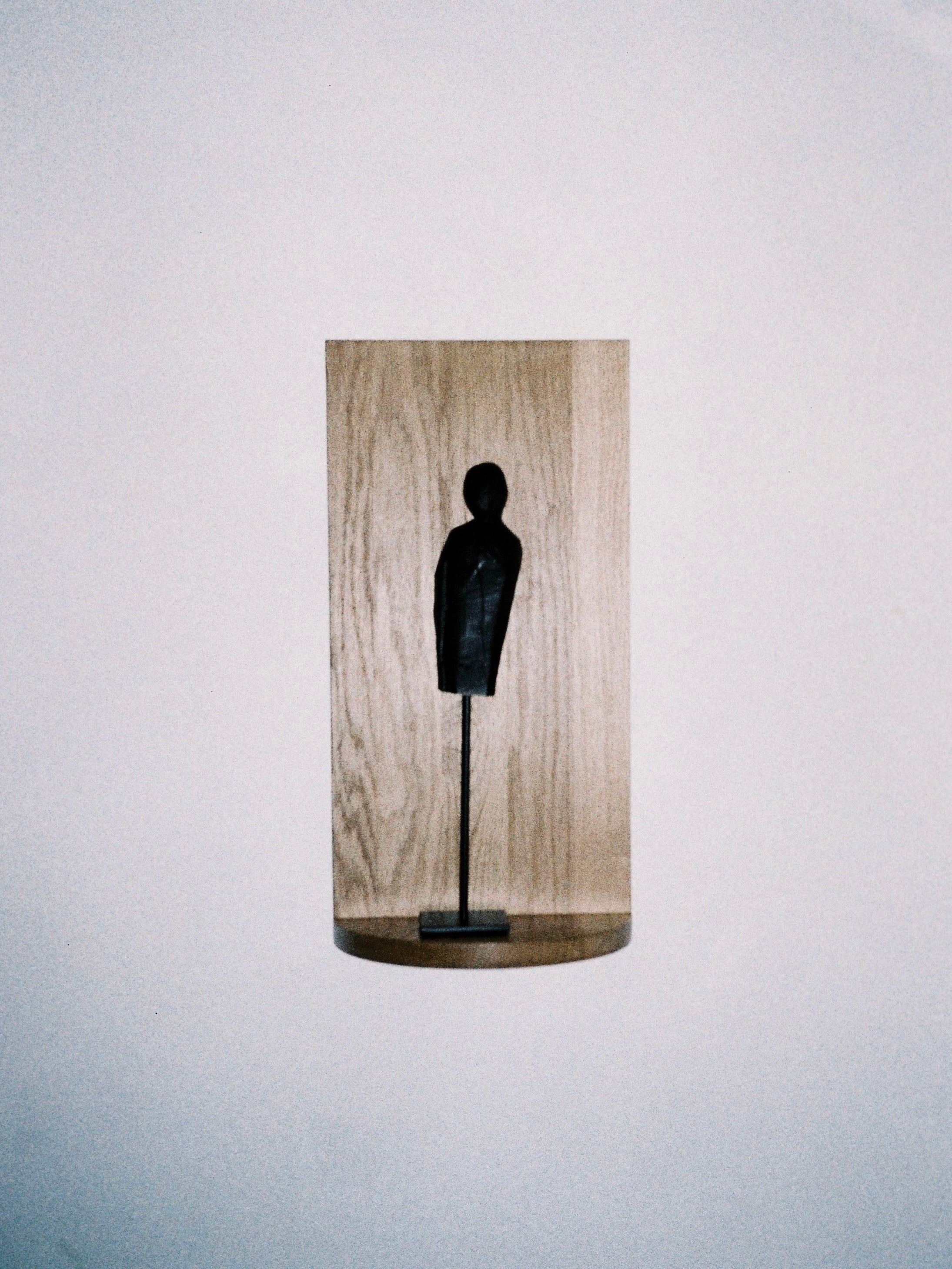 A minimalist sculpture showcasing a slender, abstract human figure in dark metal stands on a thin pedestal. Made in Italy, this piece is elegantly mounted against a light wood background and is displayed on the Megaron Shelf (Small) by COSEINCORSO in a simple white setting.