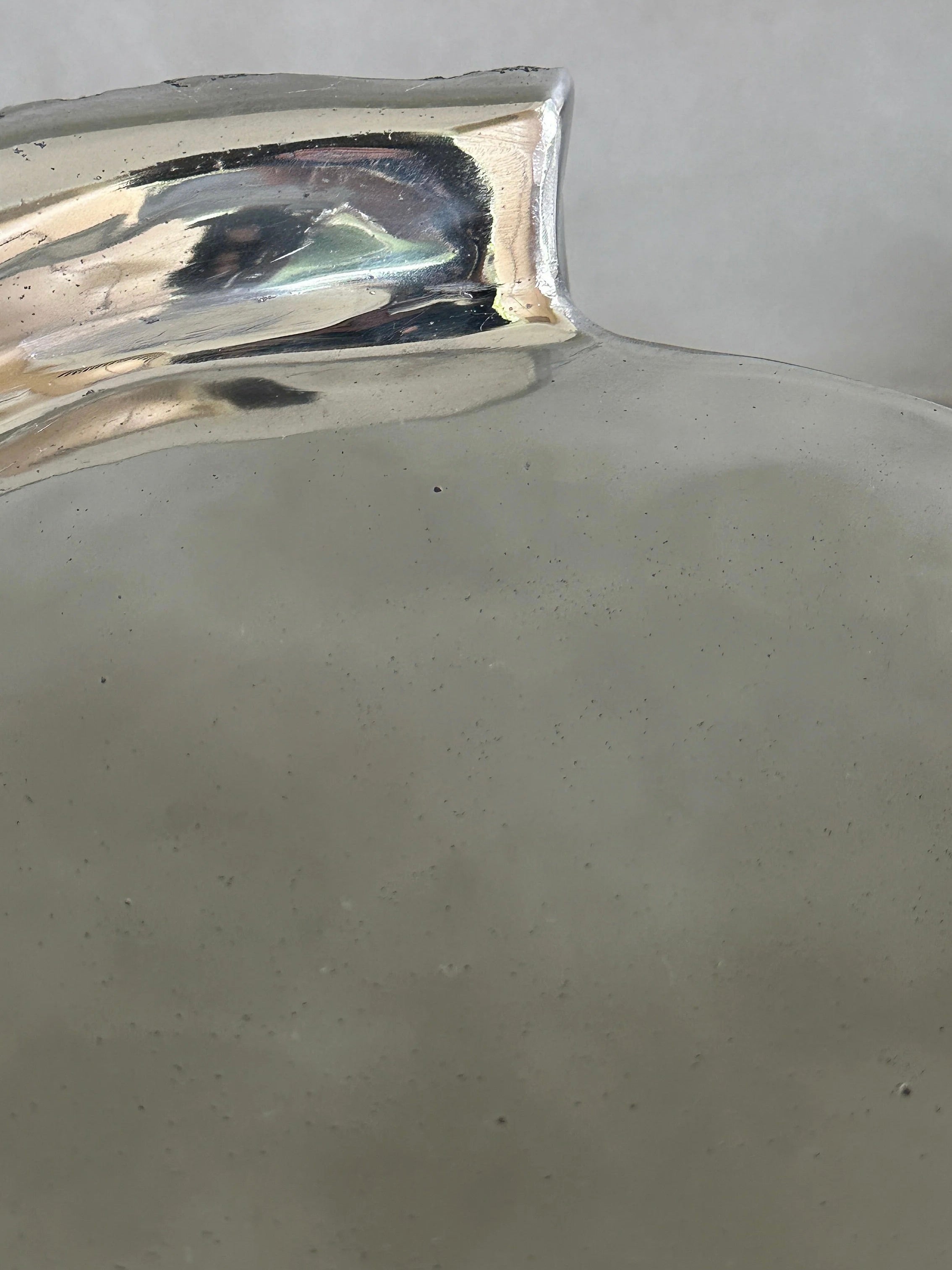 Close-up of the "Bark" Side Table by Kaytar, a shiny, silver-colored curved piece against a light gray background. Its high-gloss finish enhances the reflective surface, suggesting its decorative or functional purpose.