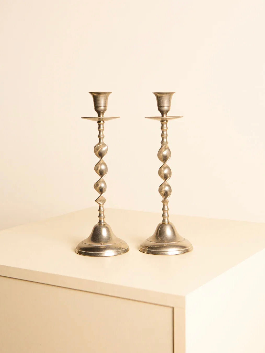 The Pair of 60's Italian Metal Candleholders by Treaptyque are arranged side by side on a light-colored surface against a simple backdrop, showcasing their twisted bodies.