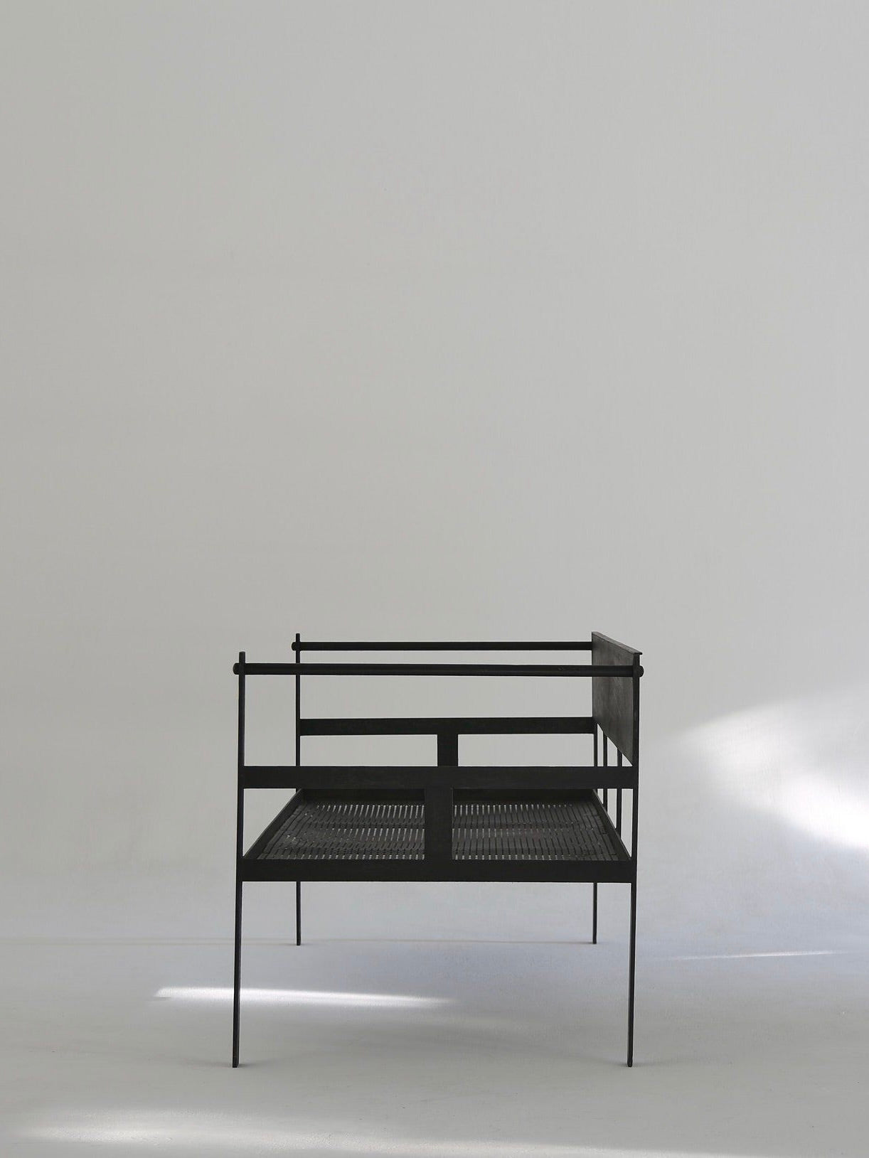 The Ancien et Jolie Modernist Lounge Set features a minimalist metal daybed with a simple frame, evoking Mathieu Mategot's style. It has a mesh-like base, set against a light background with soft shadows around it, and lacks bedding or cushions.