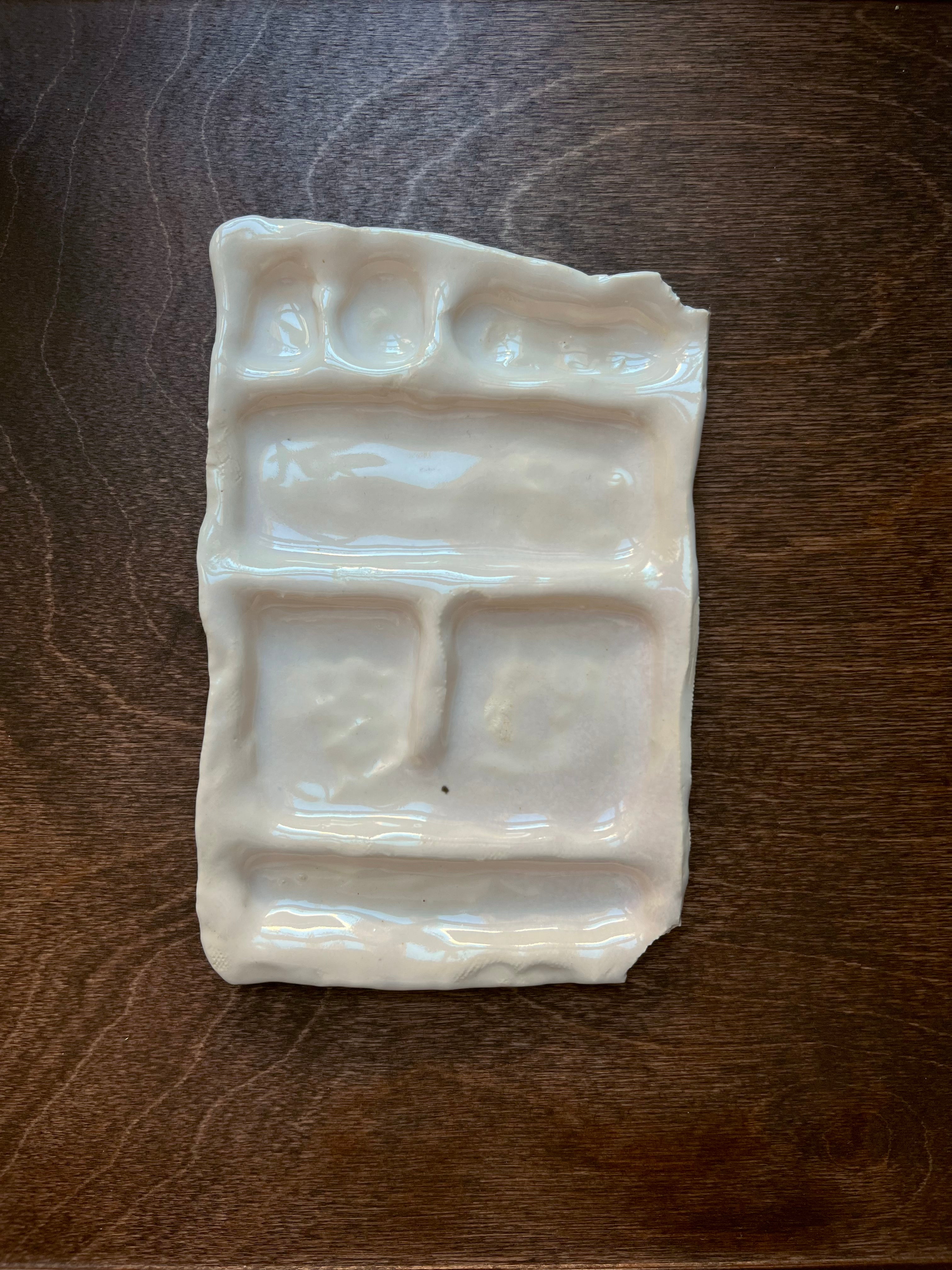 A white ceramic snack plate with six sections, photographed on a dark wood surface. The dish's shiny white glazed finish reflects light from above.