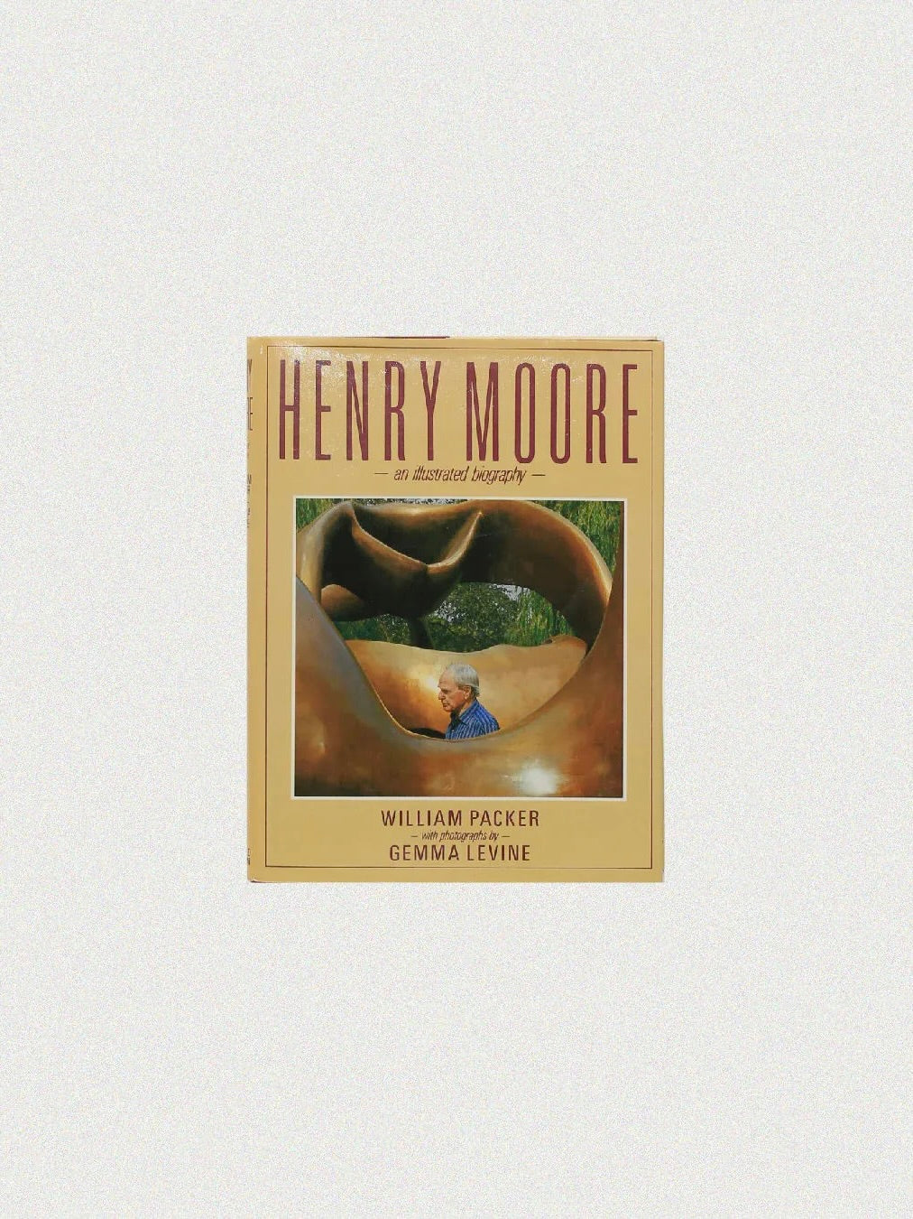 Book cover titled "Henry Moore, An Illustrated Biography" available at Boga Avante Shop. It features a photograph of the renowned British sculptor in a blue sweater among his large modern sculptures against a beige background.