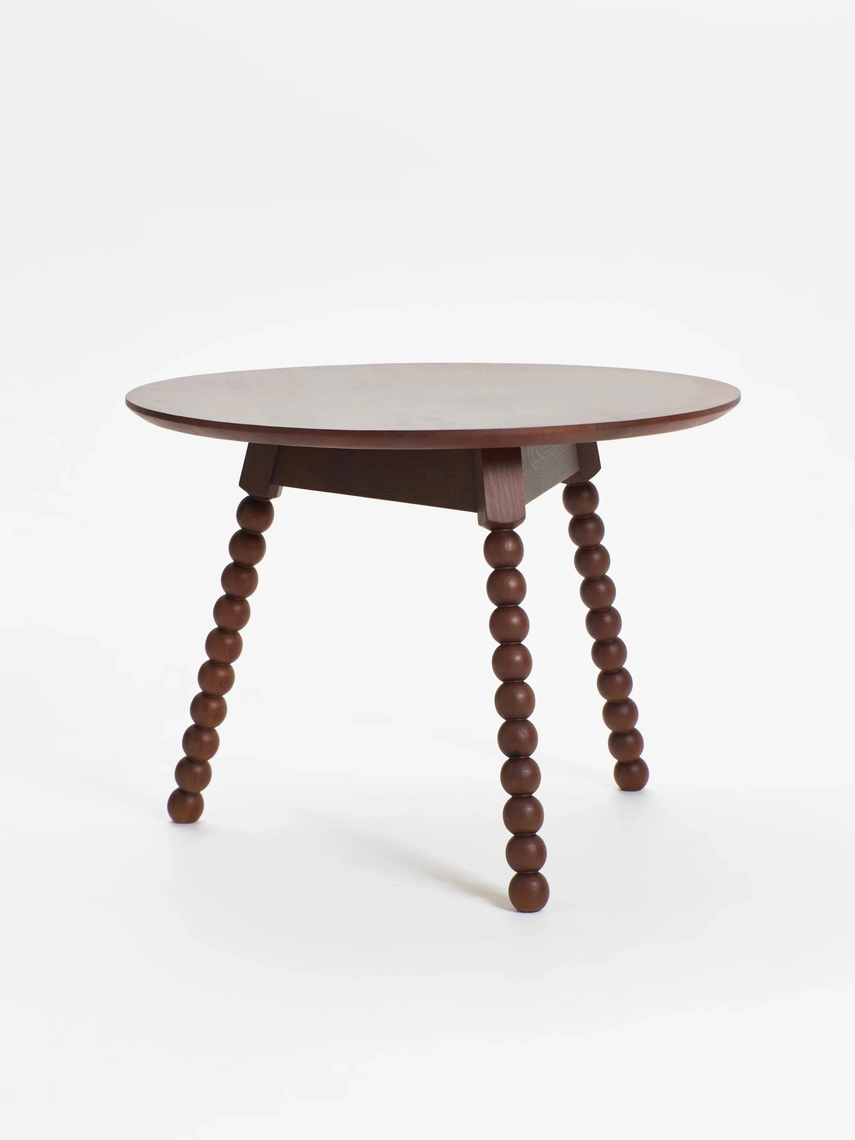 The 'Bolha' Table by Project 213A is a round wooden bistro dining table featuring a smooth top and three legs with turned wood detailing through stacked spherical segments. Crafted from solid wood, it showcases a dark brown finish and modern, minimalist design.