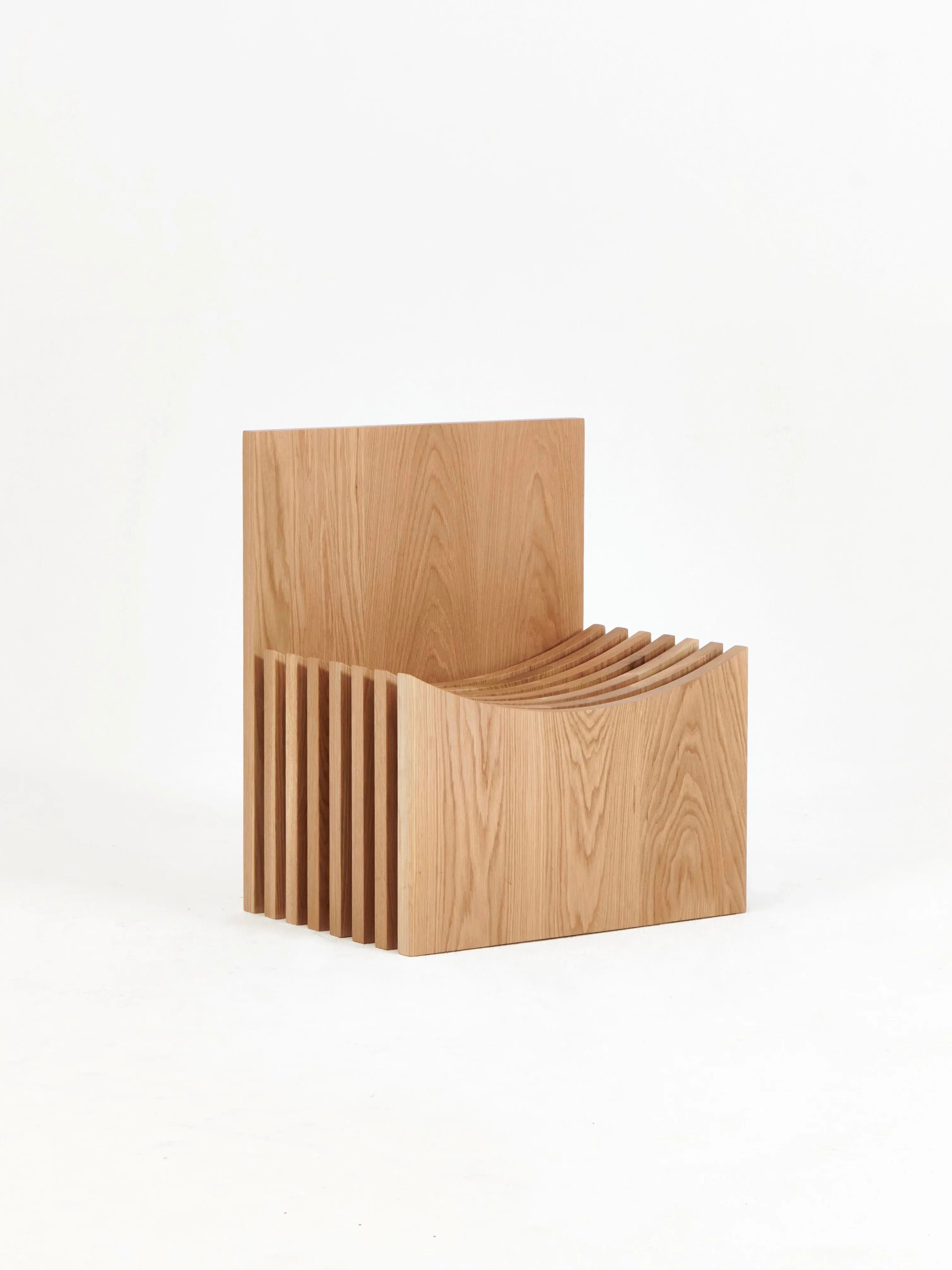 The hand-crafted Melides Chair by Project 213A is a contemporary wooden seat featuring a geometric design comprised of horizontal slats forming both the seat and backrest. It showcases a minimalist aesthetic in solid oak with a natural wood finish, all set against a plain white background.