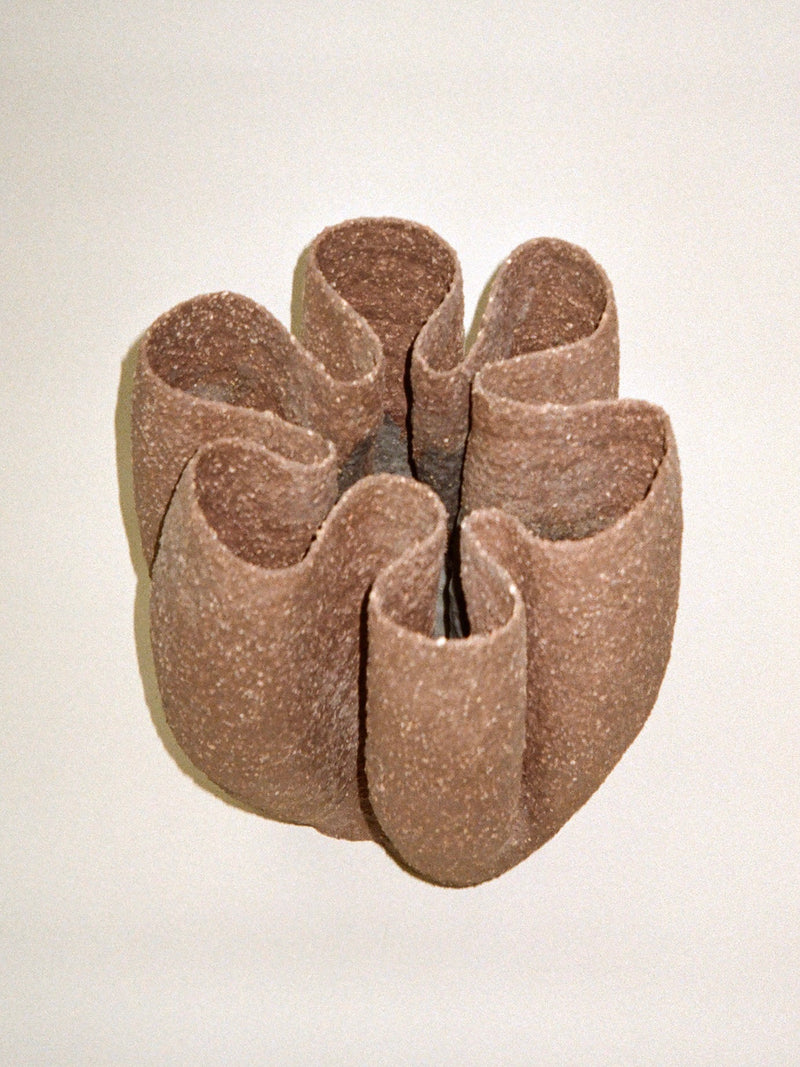 The Growing Vase n.5 by Aiste Bagdonaite is a handbuilt brown stoneware vase with six wide, curled petals and an open center, resembling a sculptural flower against a simple, light background.