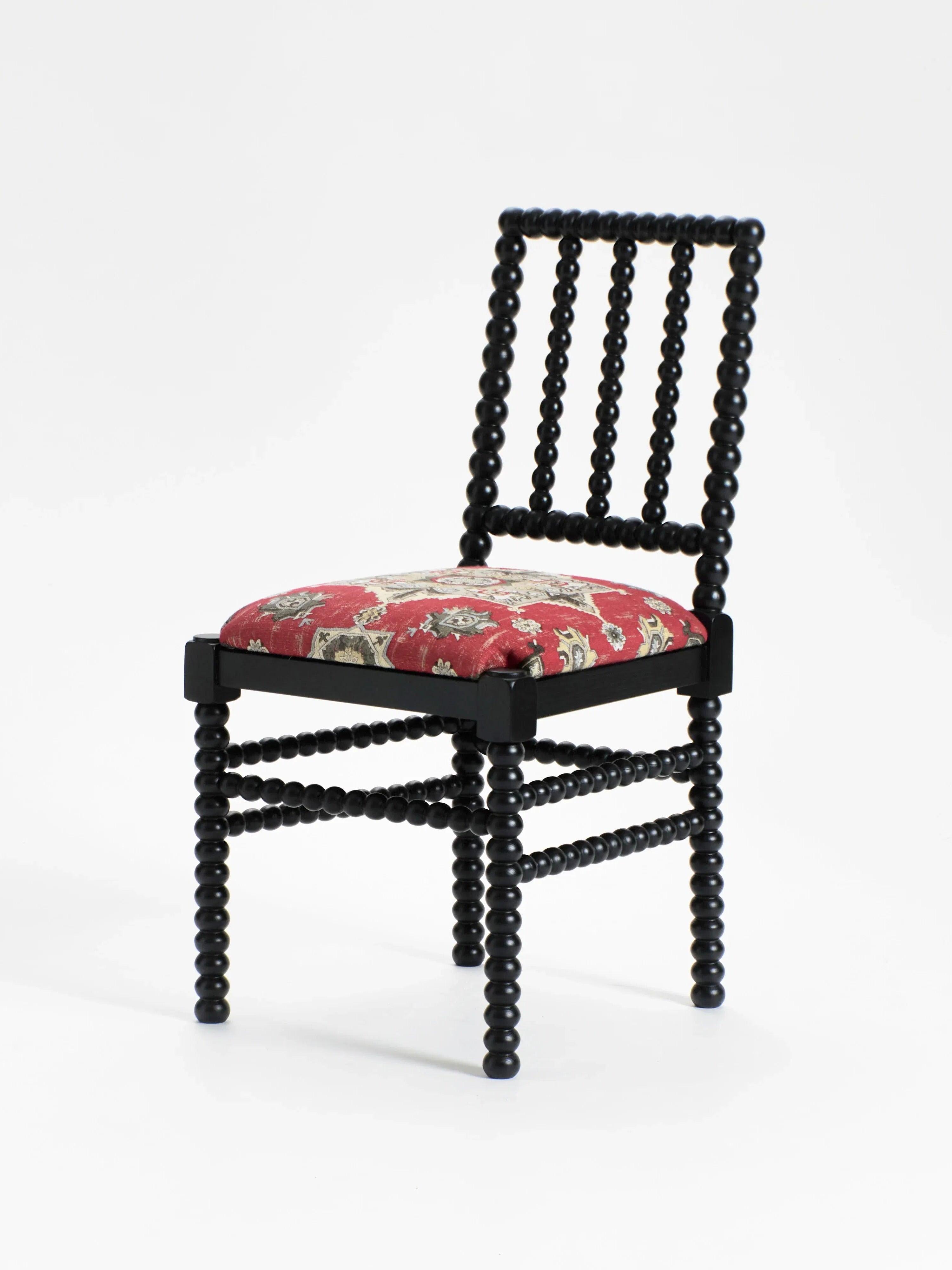 The "Bolha" Chair by Project 213A is a vintage masterpiece featuring a unique beaded design with elegant wood-turned details. Its black frame contrasts beautifully with the red floral-patterned cushioned seat, while spherical elements on the legs and back add distinctive texture and style.