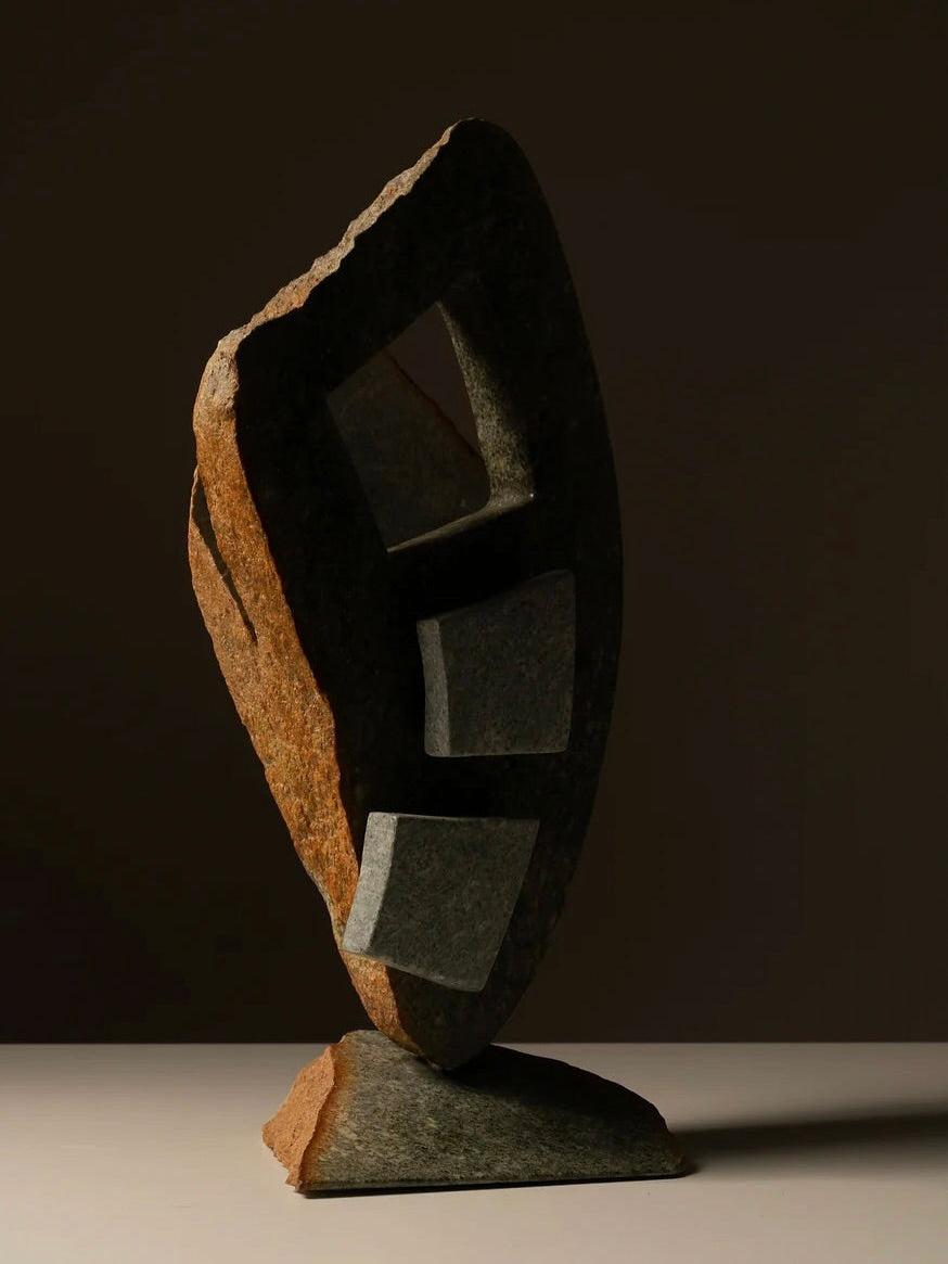 The Two-toned Abstract Sculpture by Les Objets Amsterdam is a modernist, handmade piece that stands on flat surfaces. Made from natural stone, it features an asymmetrical shape with three rectangular openings and a dark, textured finish, creating dramatic contrast against dark backgrounds.